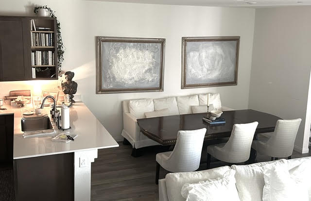 Living room with a white sofa, dark dining table, four white chairs, and two framed paintings on the wall.