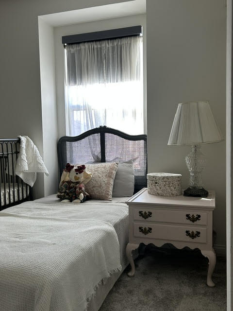 Bedroom with a bed, window with curtains, nightstand with a lamp, and decorative items.