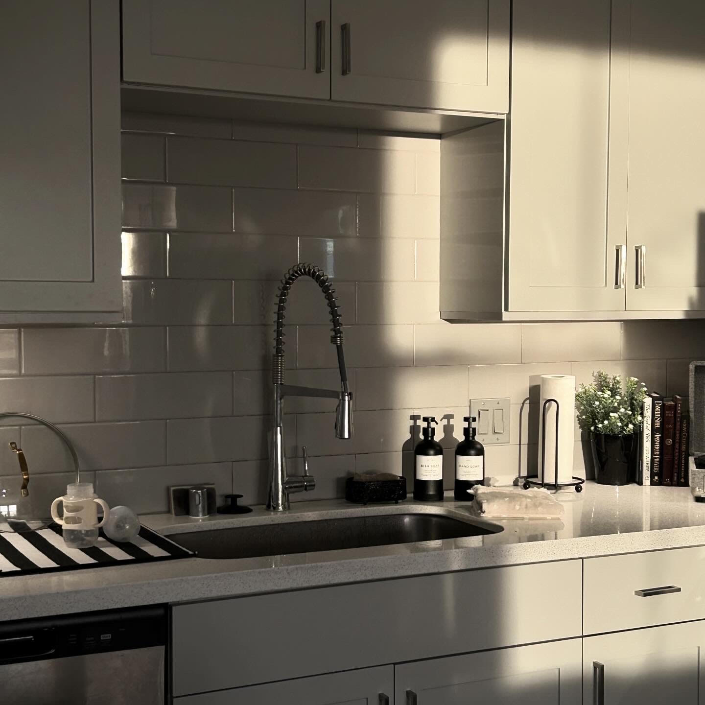 Kitchen with white cabinets, a sink with a tall faucet, and various bottles and plants on the counter.