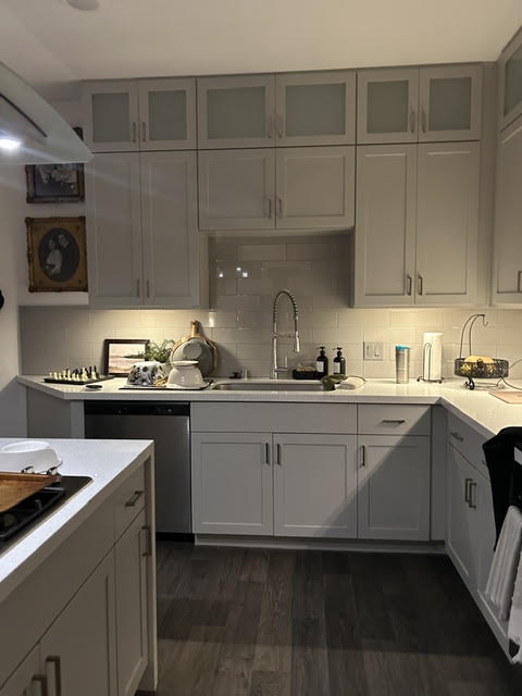 Kitchen with white cabinets, countertop, sink, and various appliances, viewed from a corner, with dark flooring.