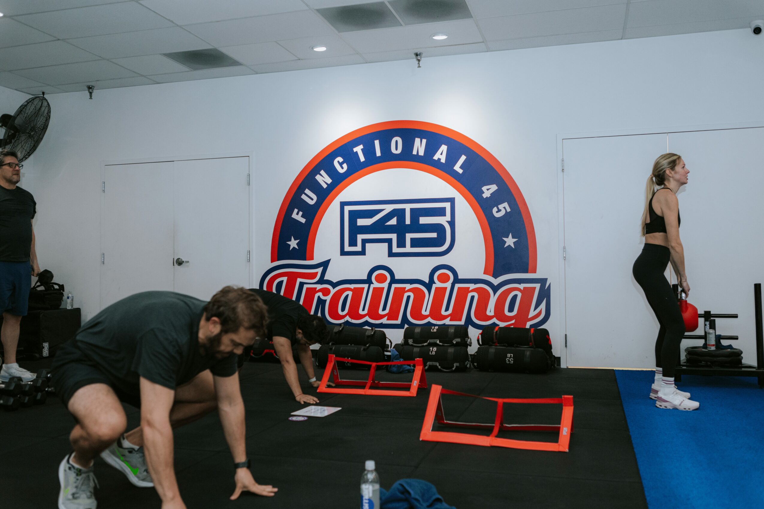 People exercising in a gym with a large logo on the wall reading 'F45 Training'.