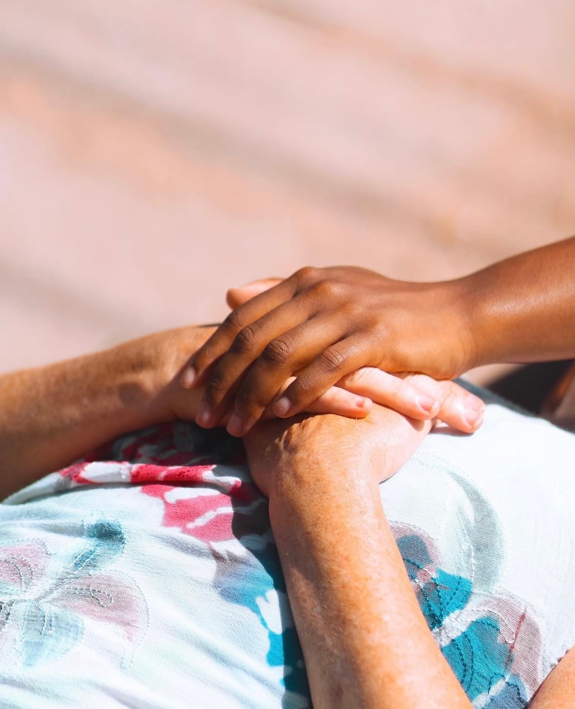 Two people hold hands, one with darker skin and the other with lighter skin, resting on a colorful fabric surface.