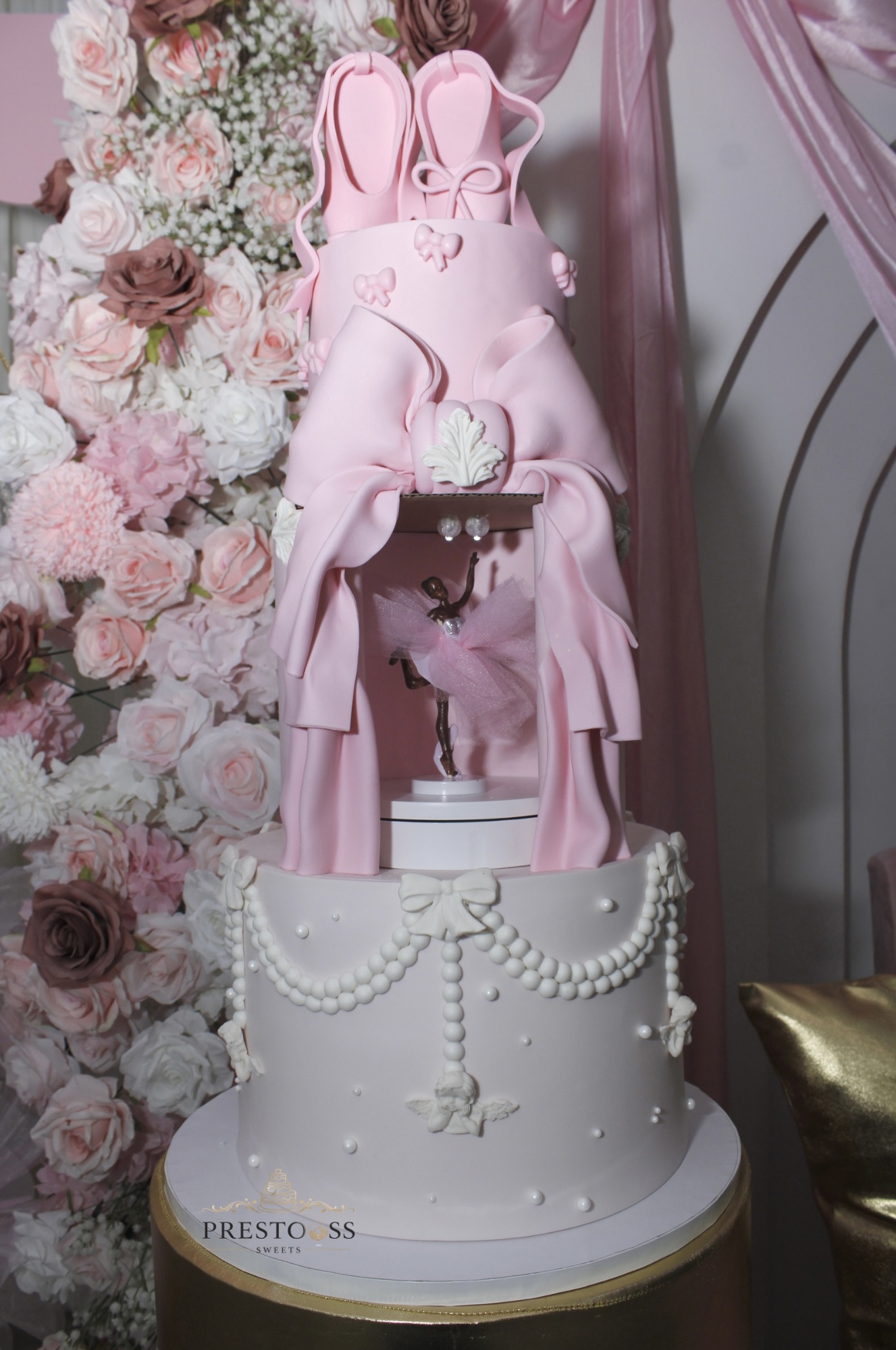 Pink bunny-shaped sculpture on a decorated cake with flowers and drapery background.