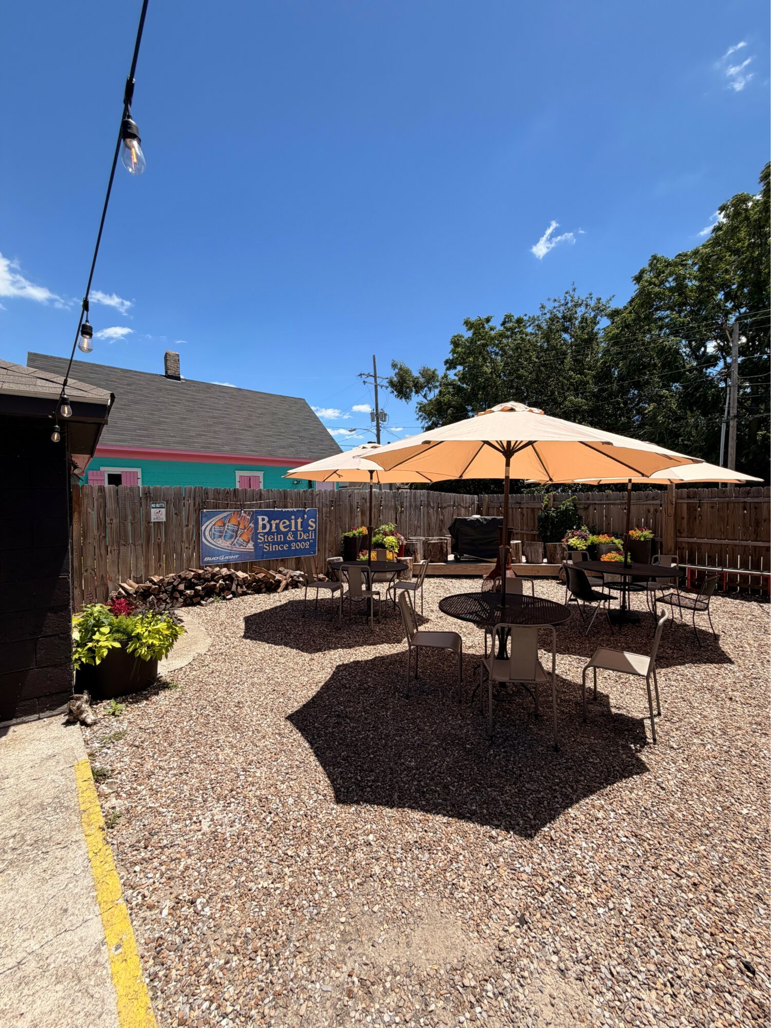 Outdoor patio with tables, chairs, and a large umbrella under a blue sky with some clouds.