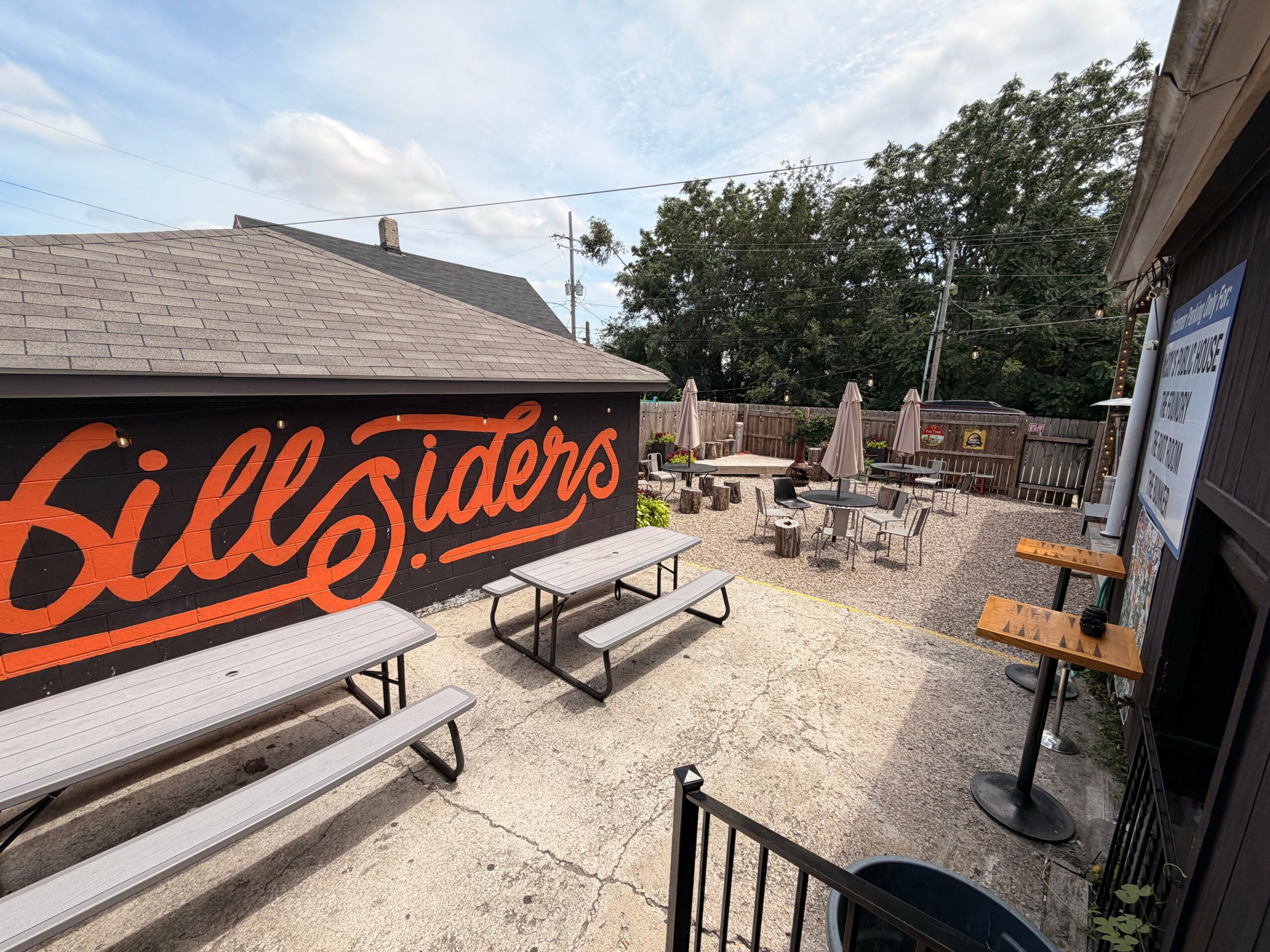 Outdoor seating area with tables, chairs, and umbrellas, next to a building with a large sign reading 'Bill Siders'.