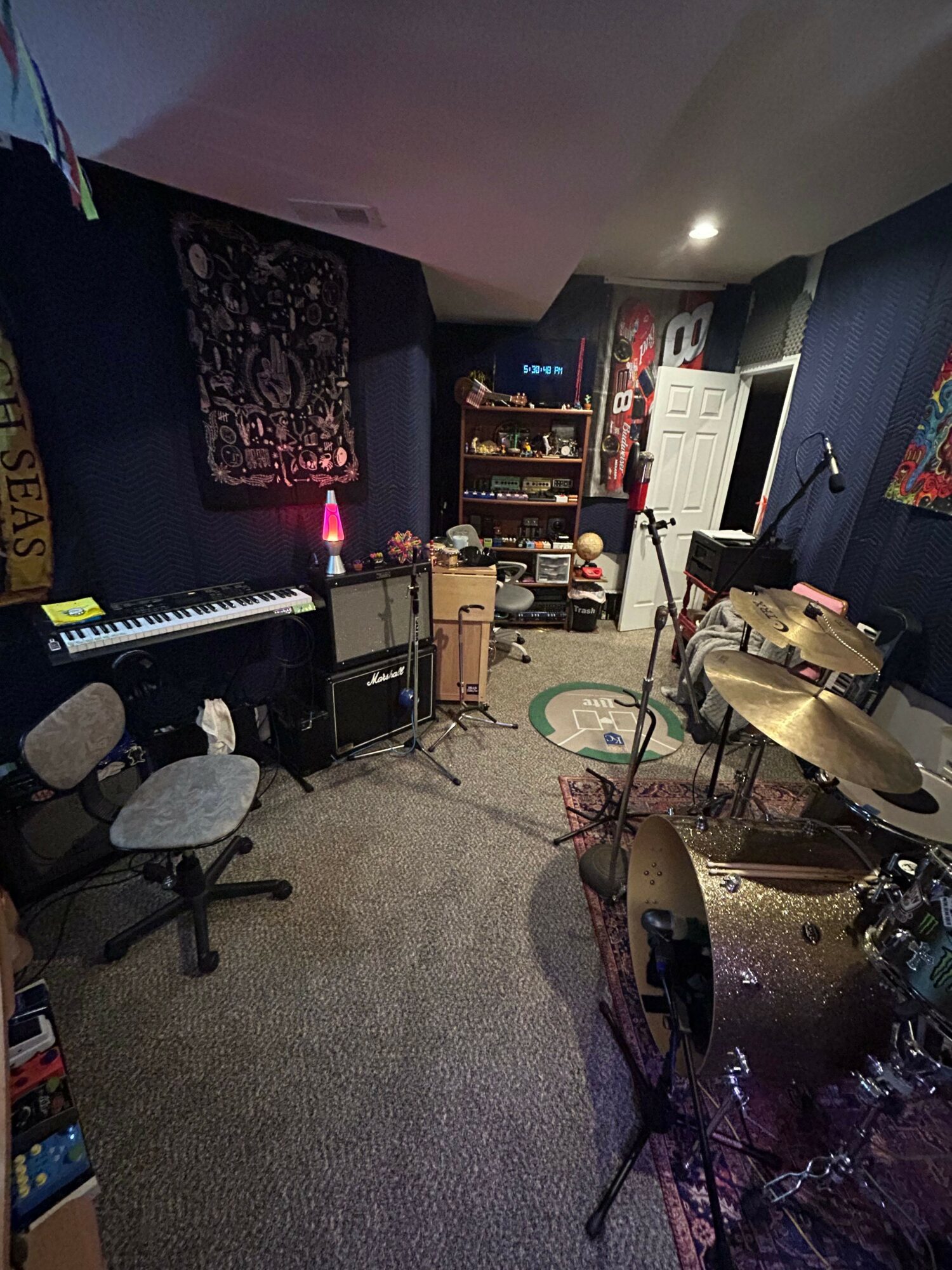 Music equipment and instruments in a dimly lit room with a dark wall and carpeted floor.