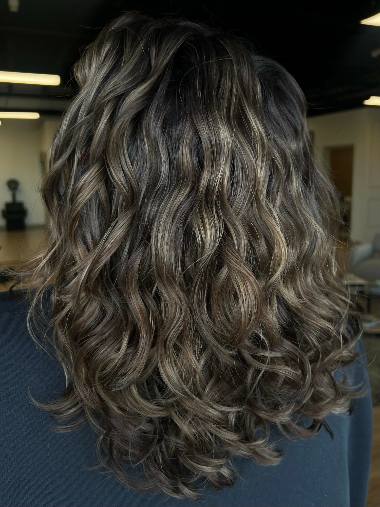 Back view of a person with long, wavy, multi-toned hair in shades of blonde and brown.