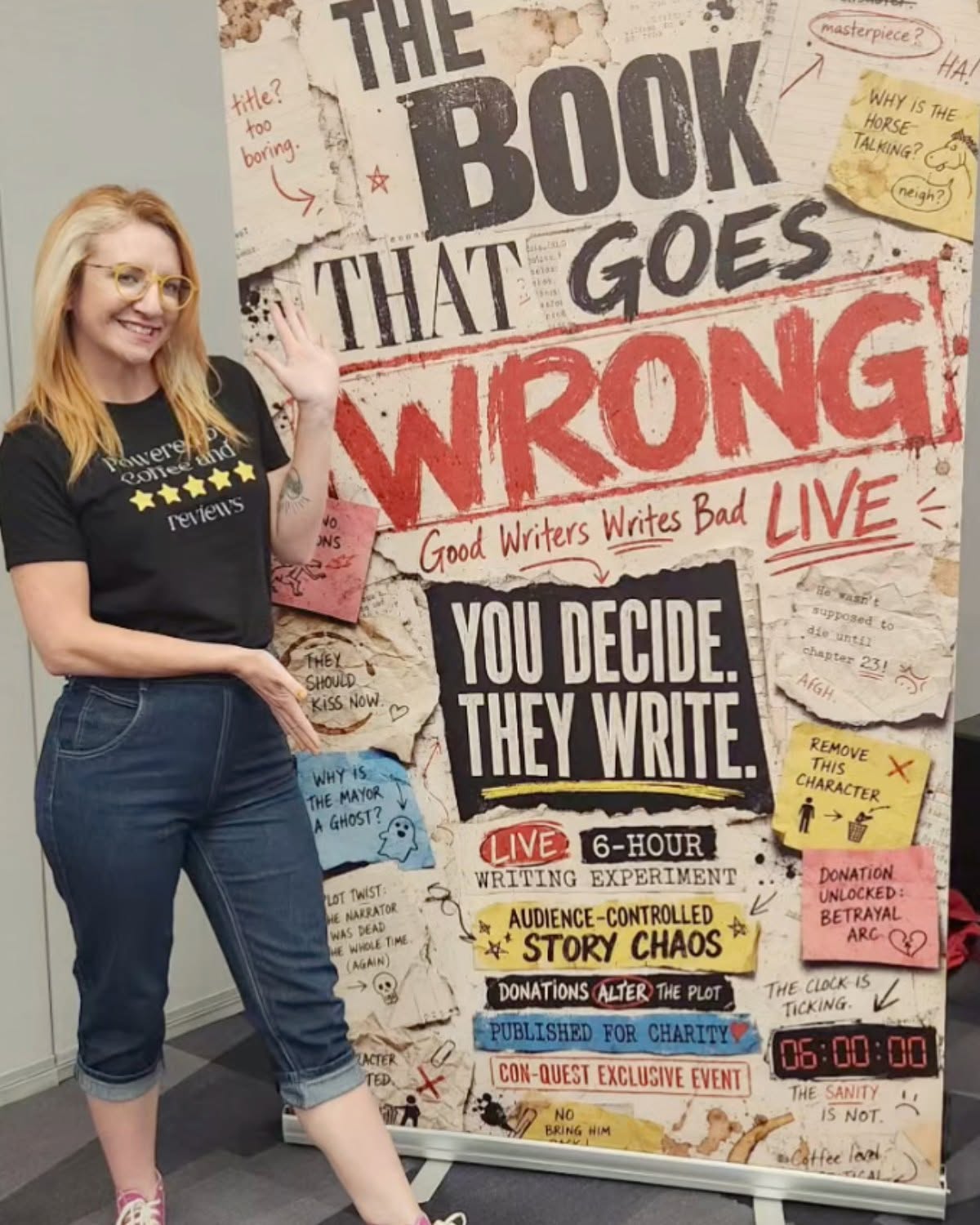 Woman with glasses and long hair standing next to a colorful poster with text and drawings, smiling, wearing a black t-shirt and jeans.