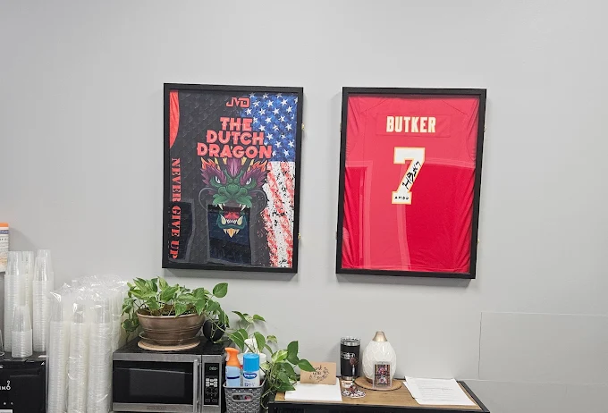 Two framed sports posters on a gray wall, one for Dutch Dragon and one for a player named Butker, with a counter and plants below.