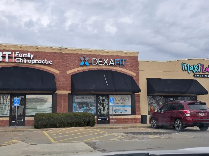 Shopping plaza with storefronts for Family Chiropractic, DEXAFIT, and MaxL. A red car is parked in front, and the sky is cloudy.
