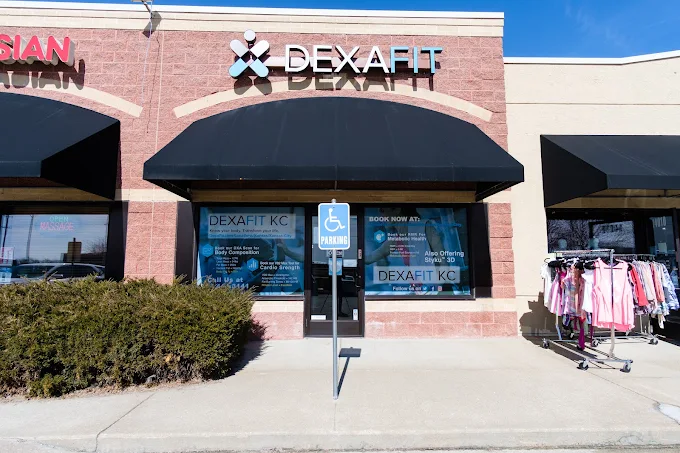 storefront with DEXAFIT sign, black awning, window displays, and clothing racks outside, under a clear blue sky