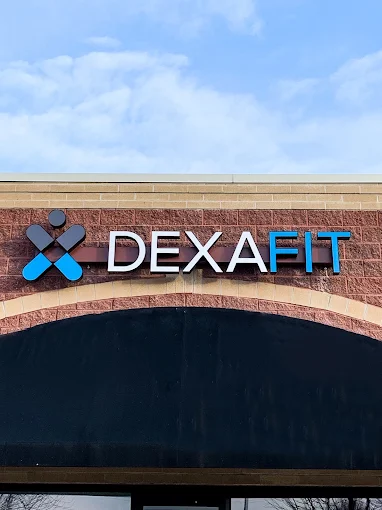 Sign with the text 'DEXAFIT' on a brick building, under a blue sky with clouds.