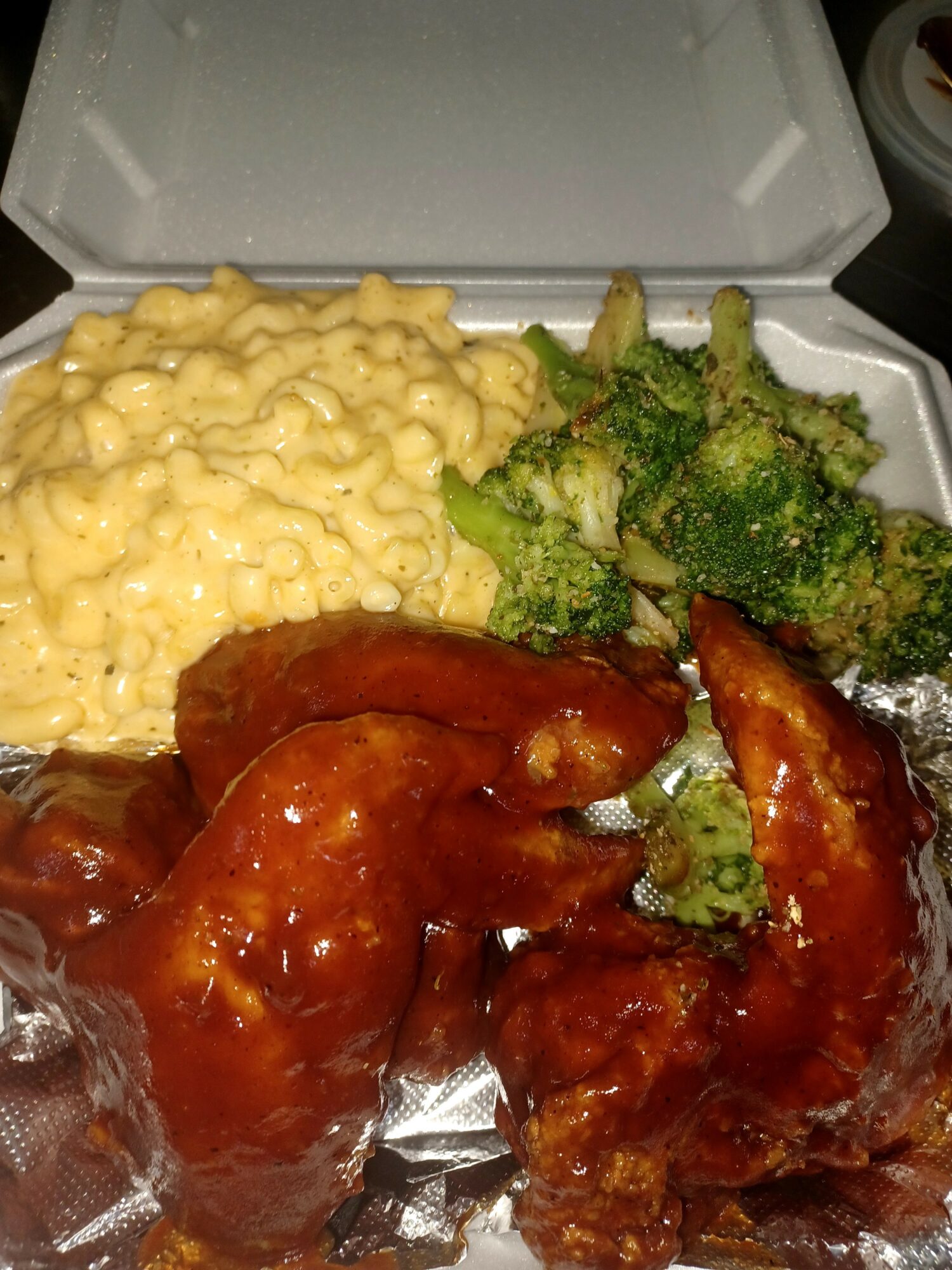 Takeout container with macaroni and cheese, broccoli, and glazed chicken wings, all inside a foam box.