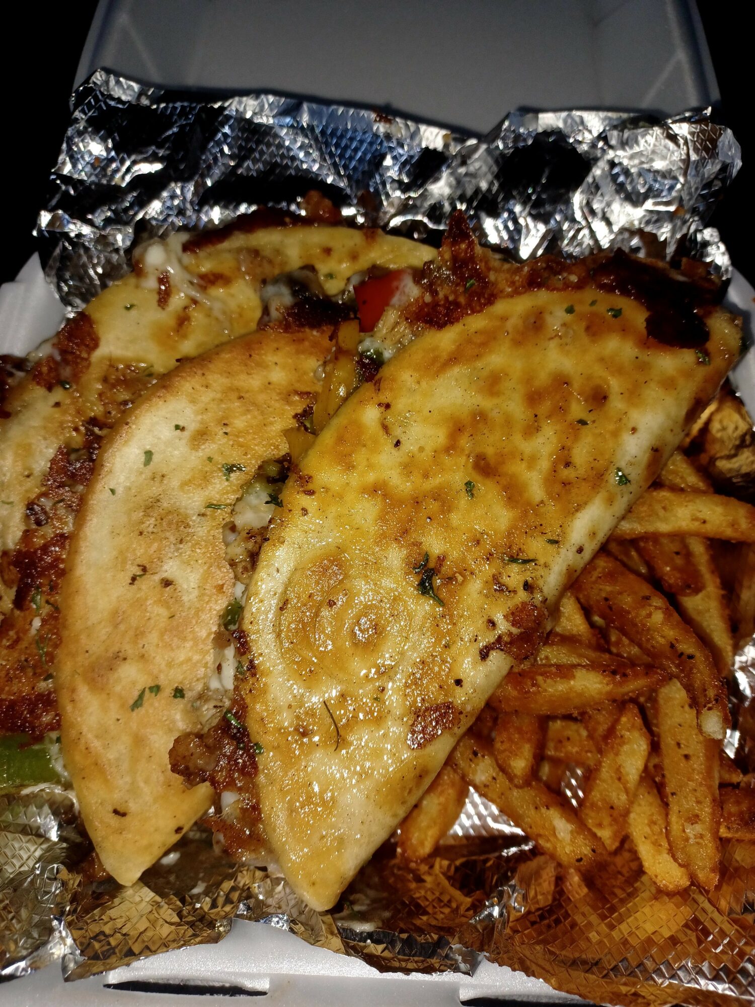 Two grilled fish fillets with herbs, French fries, and a foil-wrapped item in the background.