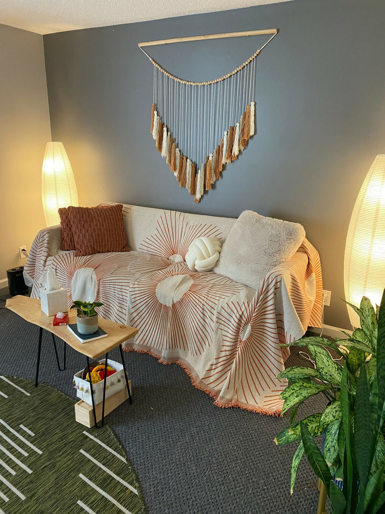 Living room corner with a sofa, blanket, side table, and wall decoration, viewed from the side.