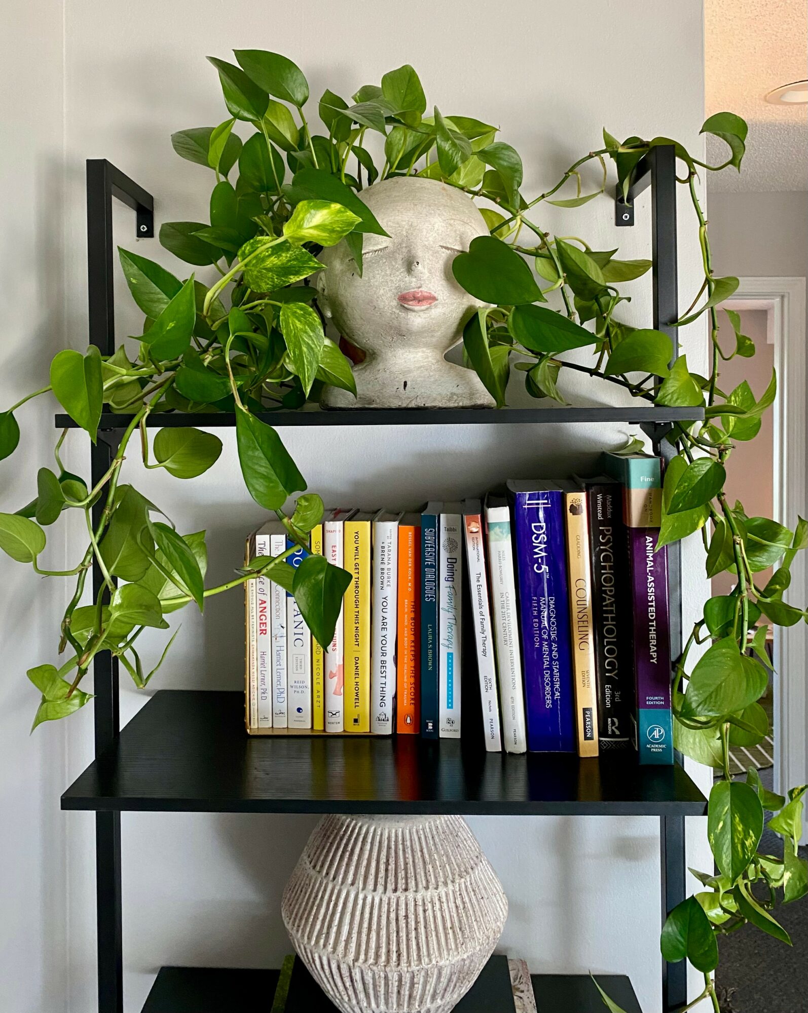 Decorative shelf with a plant, a white head-shaped planter, and books, against a light-colored wall.