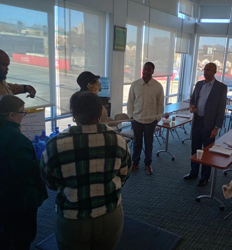 Group of people standing and talking in a bright room with large windows and tables.