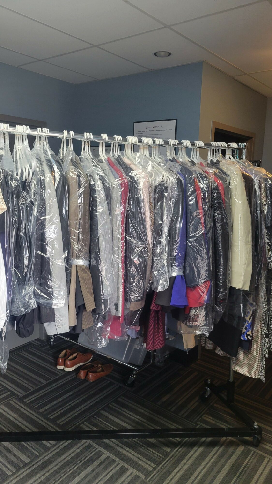 Clothing items hanging on a rack, wrapped in plastic, in a retail store or storage area.