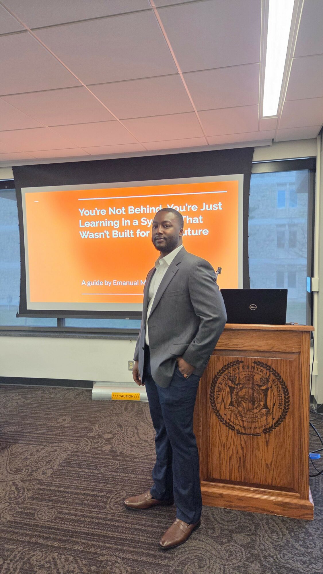 Man in a suit standing in front of a presentation screen in a conference room.