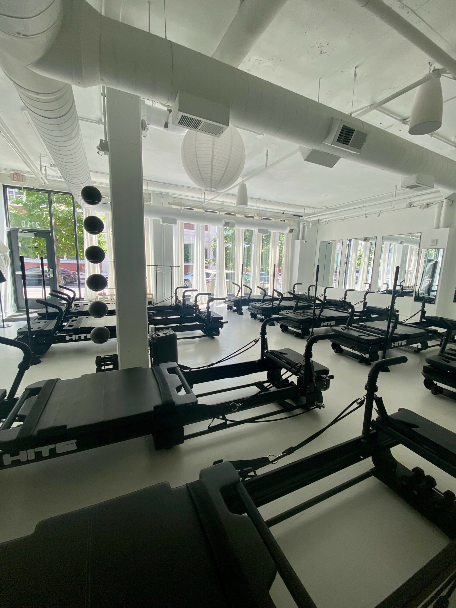 Pilates studio with reformer machines, large windows, and ceiling ventilation, bright and spacious interior.