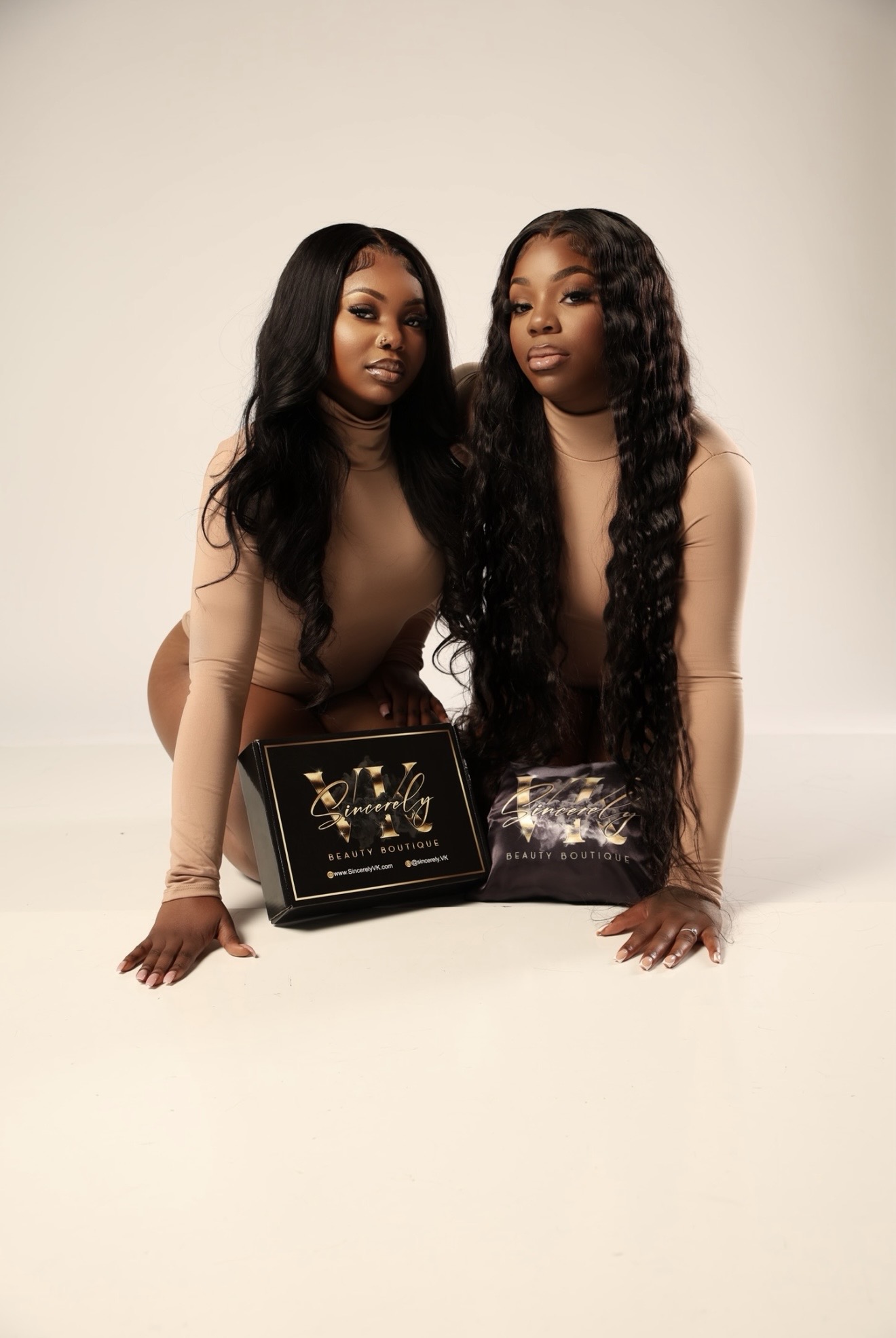 Two women with long, wavy black hair pose together, holding awards, against a plain background.