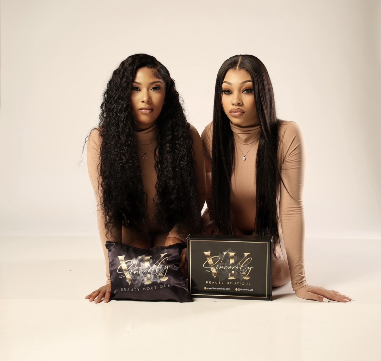 Two women with long hair sit at a table with awards and a plaque, against a plain background.