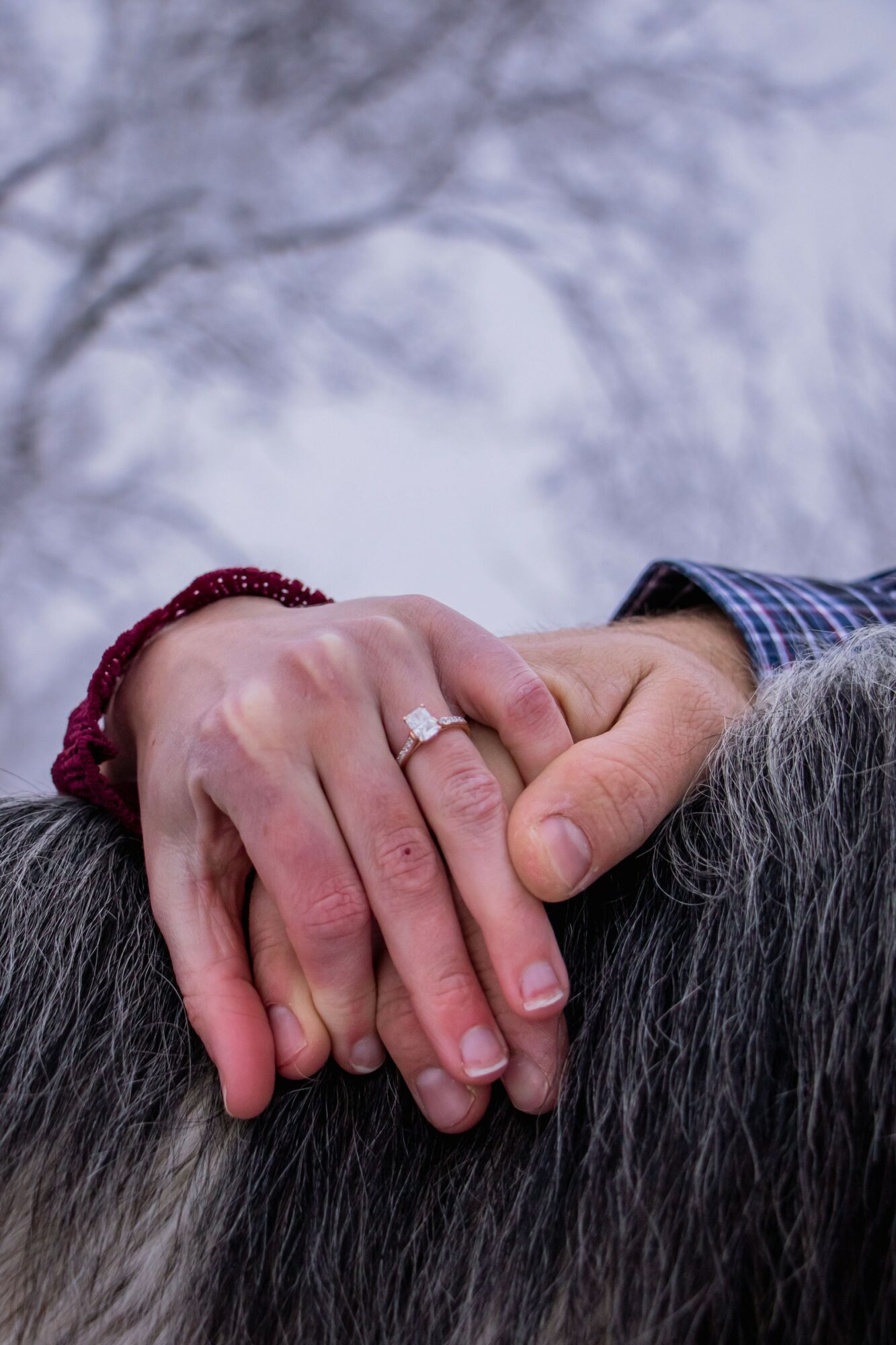 Two hands clasped together, one with a ring, against a blurred outdoor background with trees.