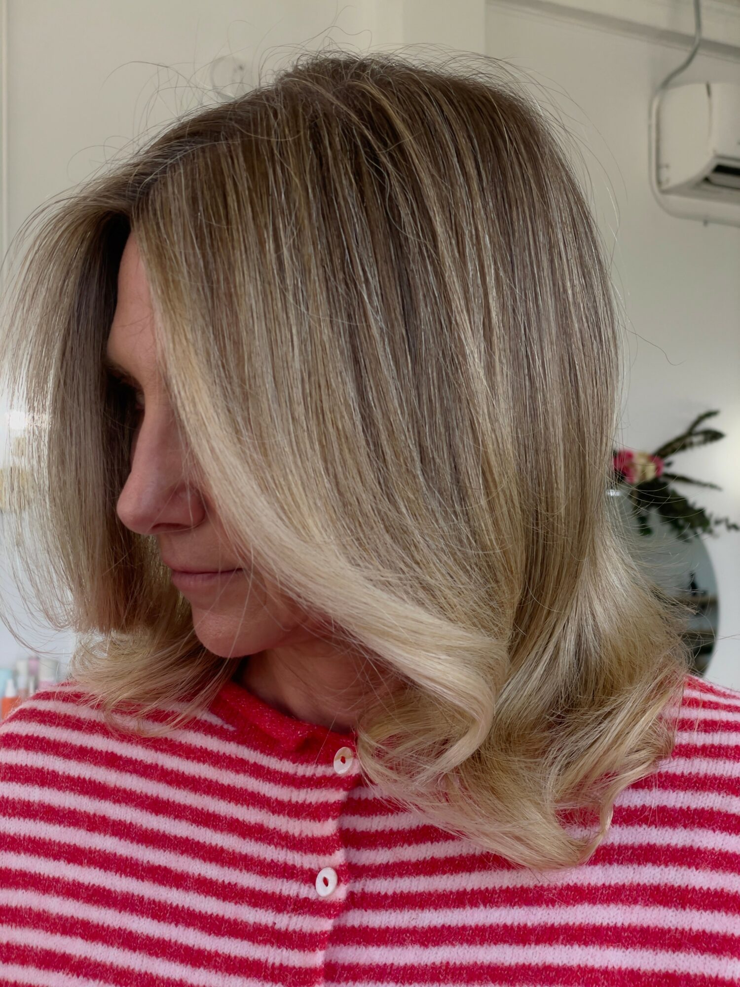 Woman with shoulder-length blonde hair wearing a red and white striped shirt, facing left, indoors.