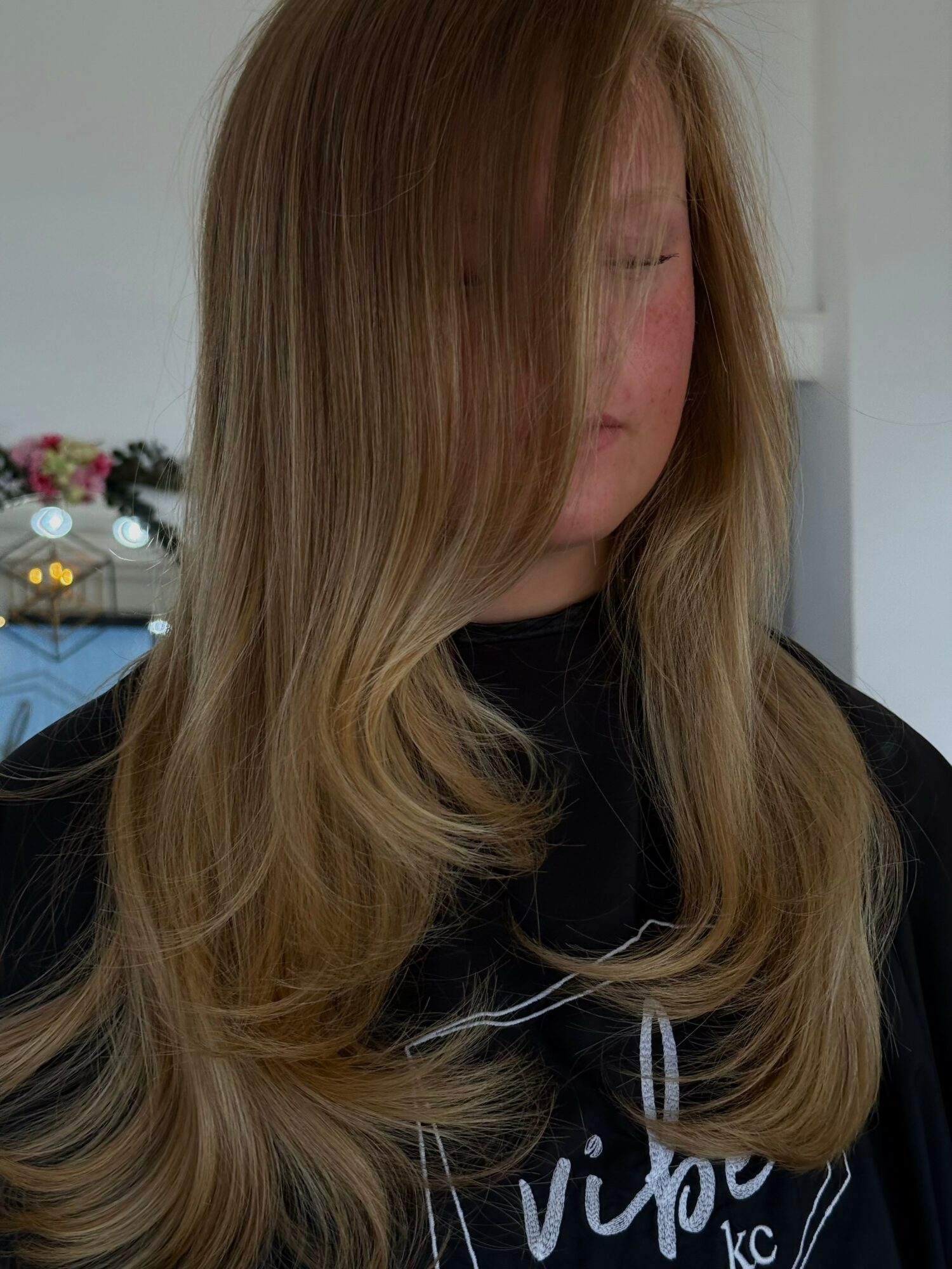 Woman with long, wavy hair covering part of her face, standing indoors with a blurred background.