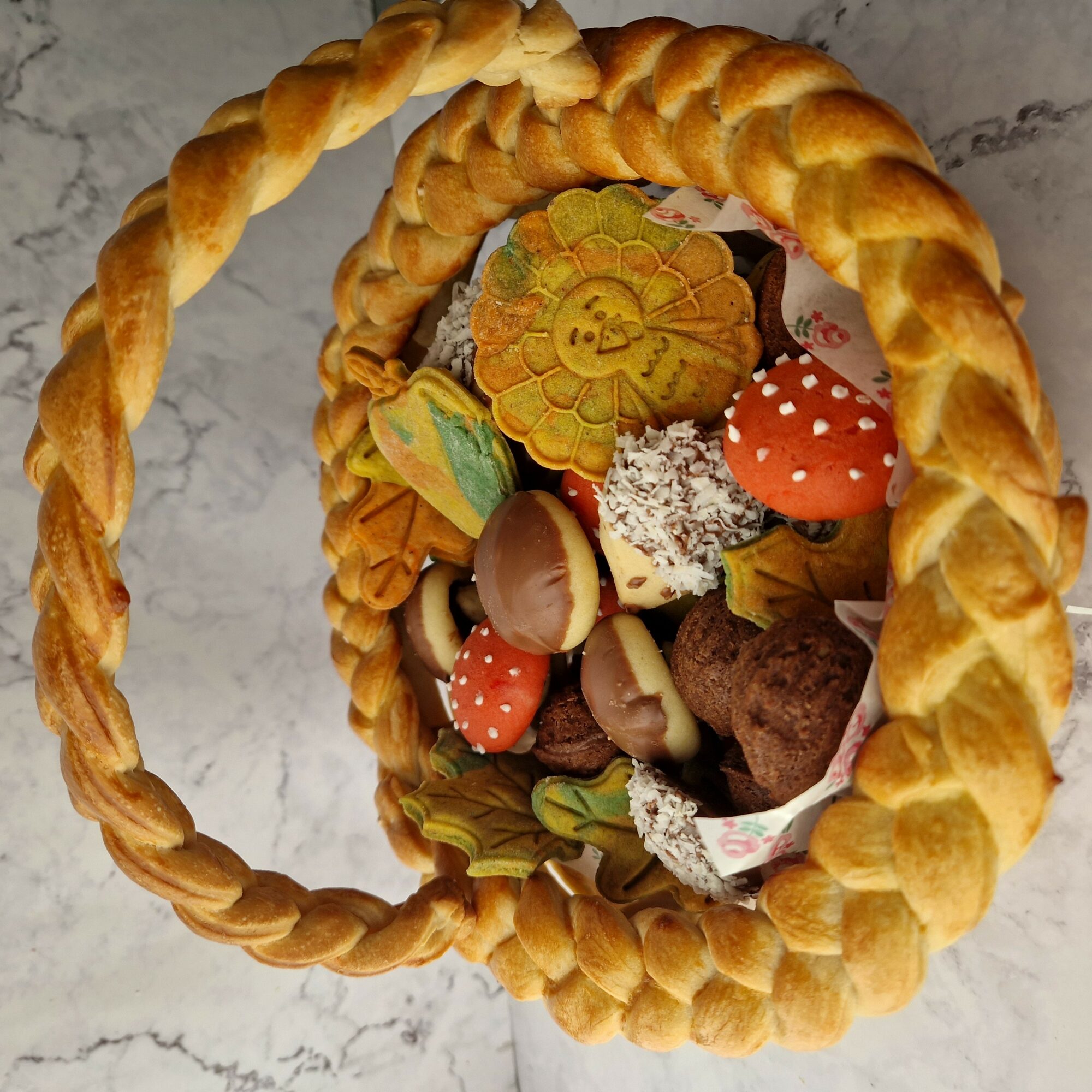 Basket filled with decorated cookies and chocolates, on a marble surface.