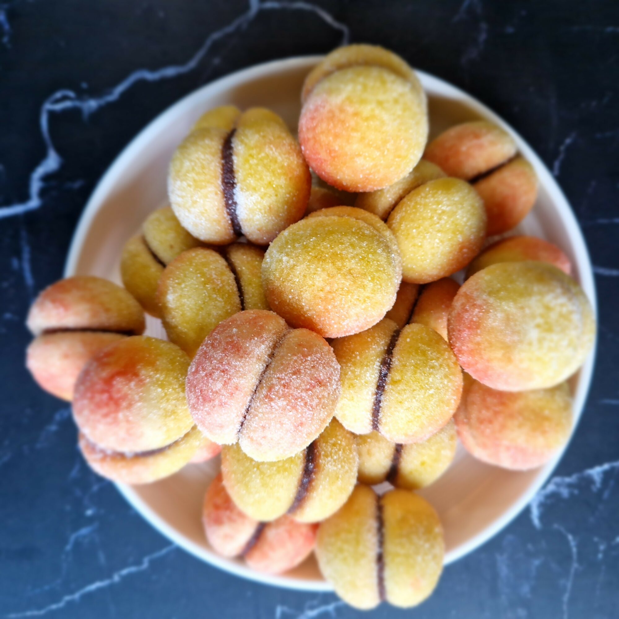 A bowl filled with small, round, peach-colored cookies with purple lines, on a dark surface.