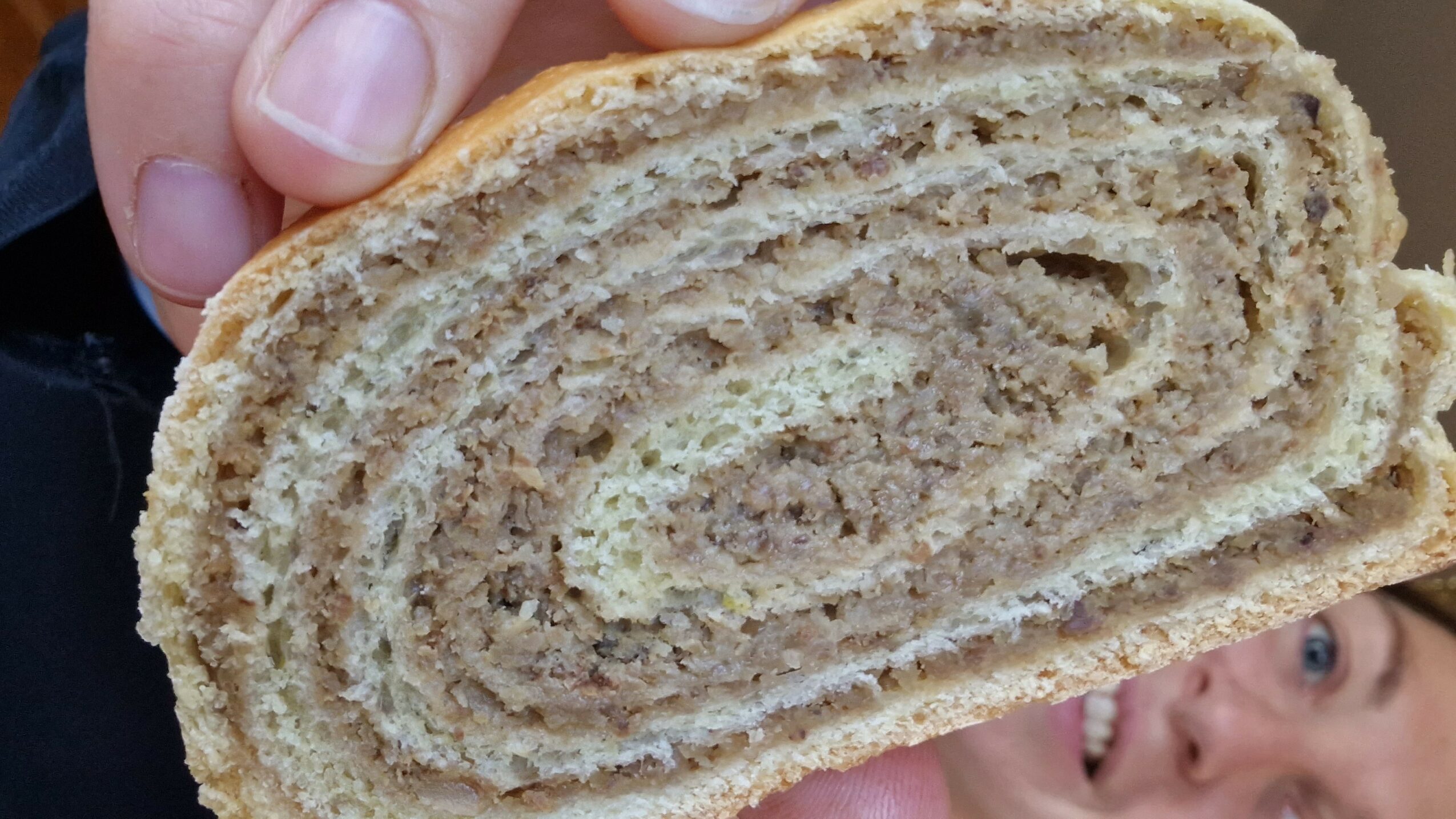 Person holding a slice of swirled bread or pastry, with part of their face visible in the background.