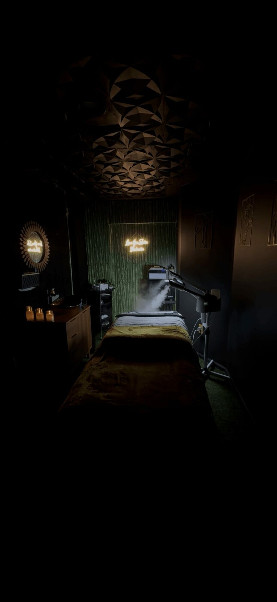 Dark room with a bed, medical equipment, and a window with light, ceiling with geometric patterns, and a chandelier.