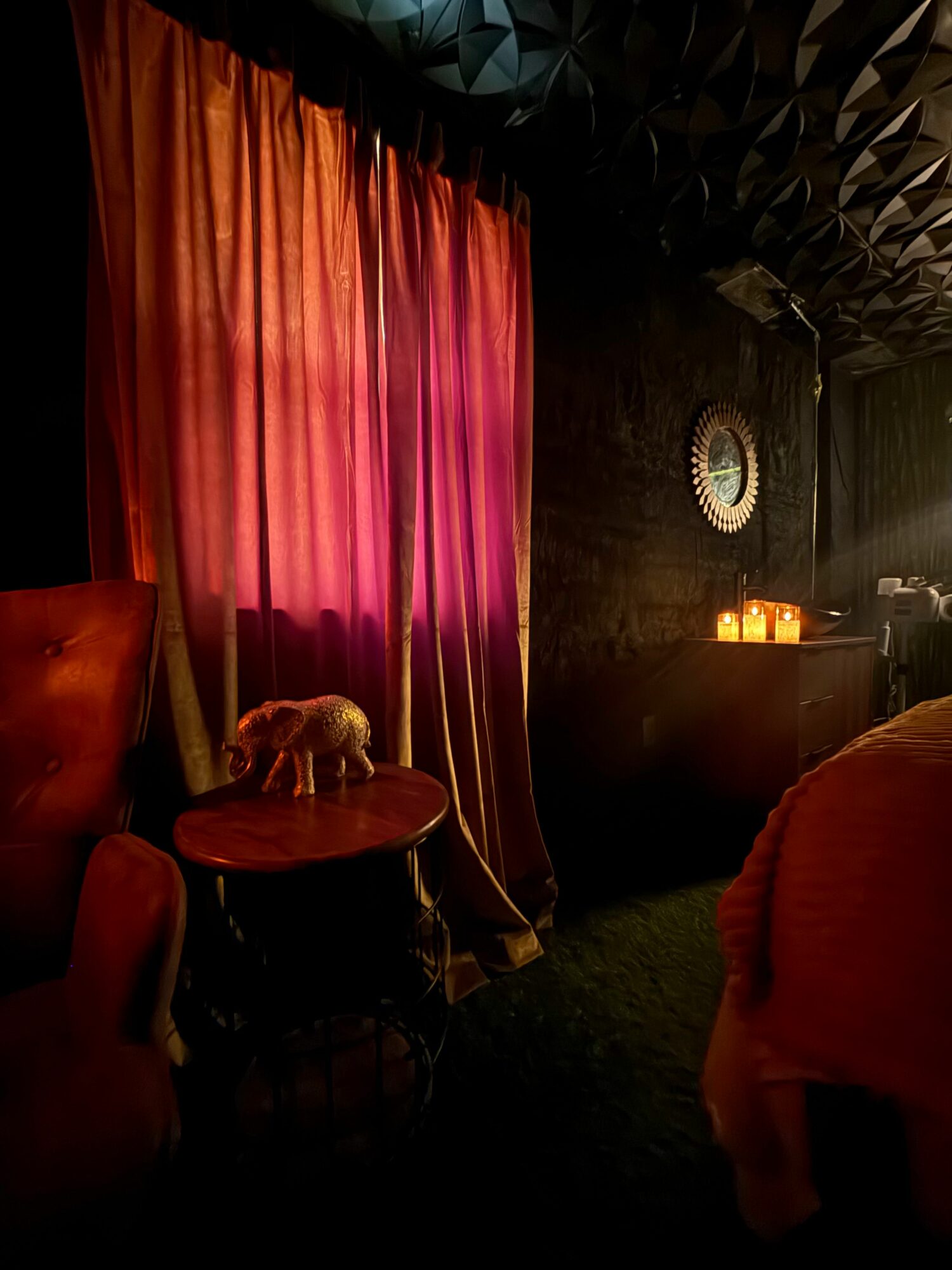Person sitting at a table with a red curtain in the background, dimly lit indoor setting.