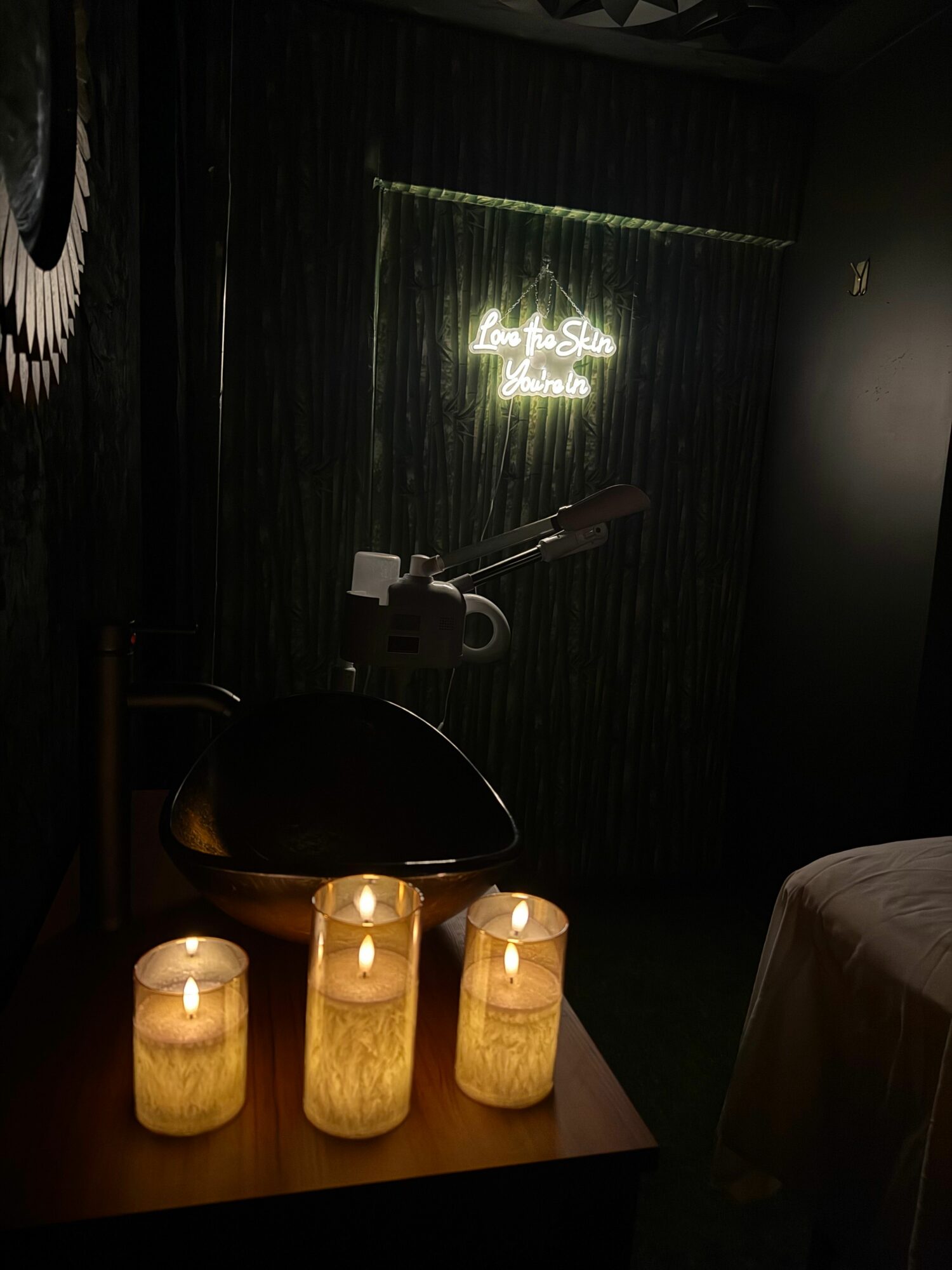 Interior scene with a window, a lamp, and candles on a table, viewed from the side, with dark curtains and a neon sign.