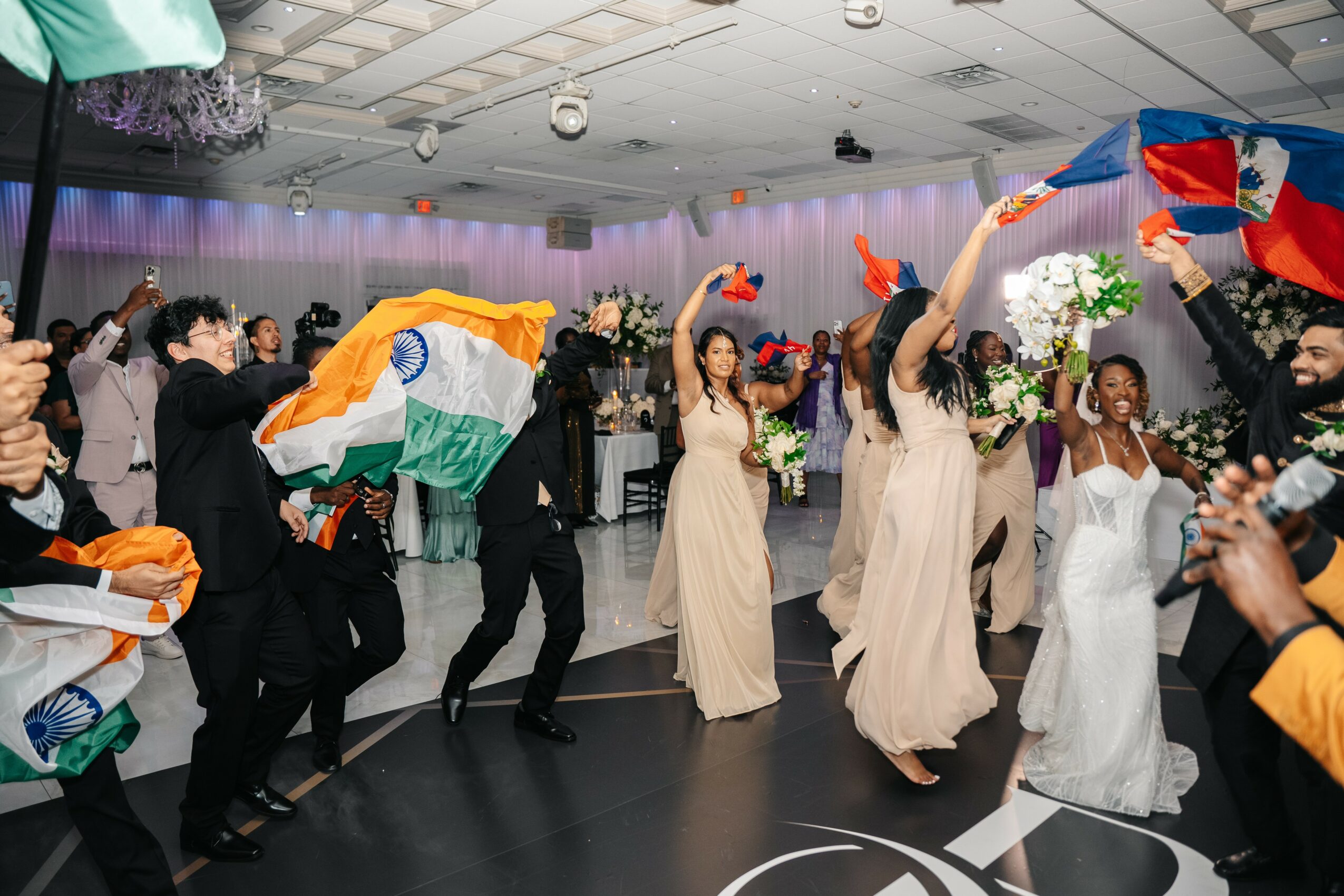 People dancing and celebrating at a wedding reception with colorful decorations and floral arrangements.