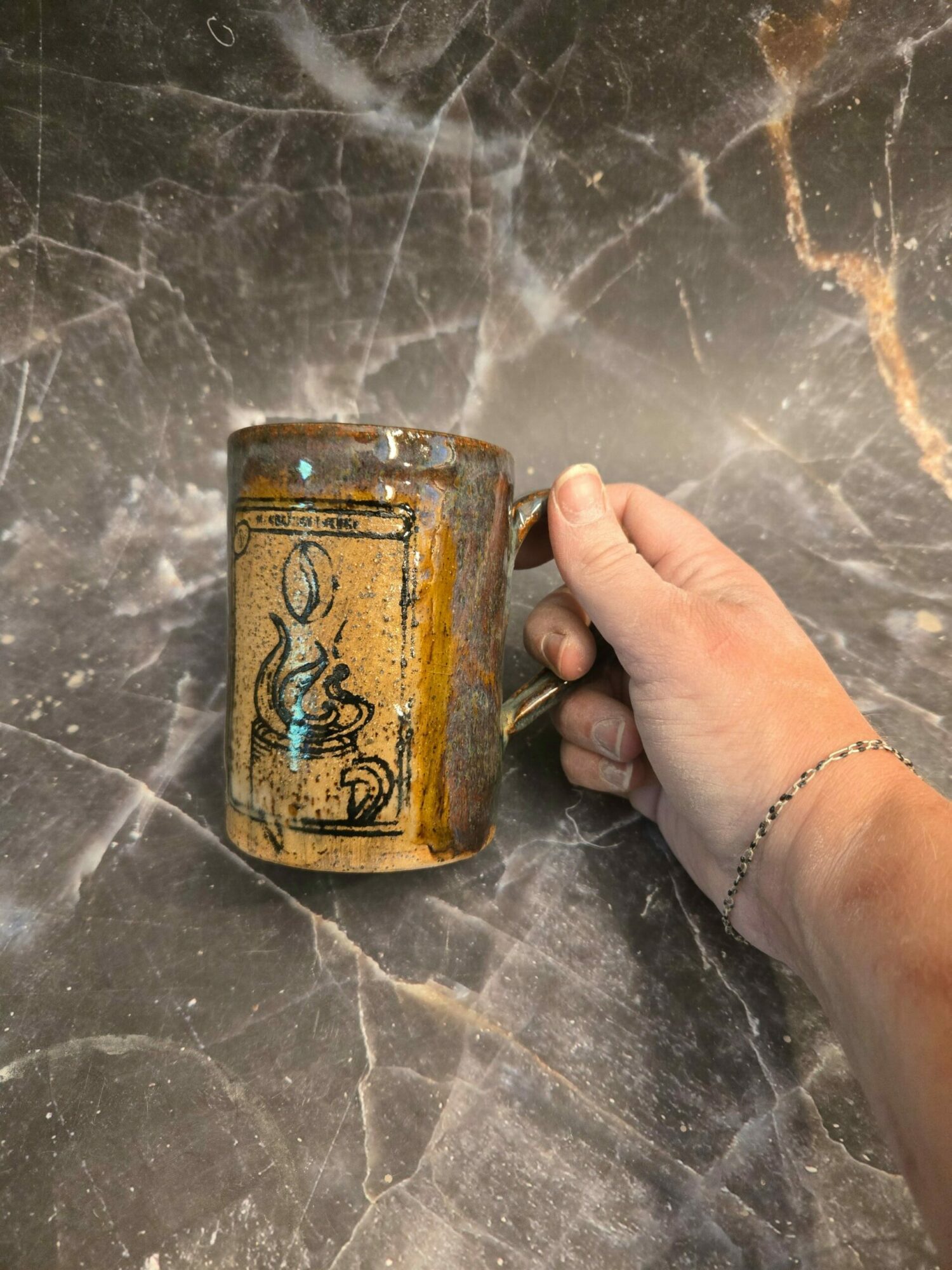Hand holding a small, cylindrical, yellowish object with black markings on a dark marble surface.