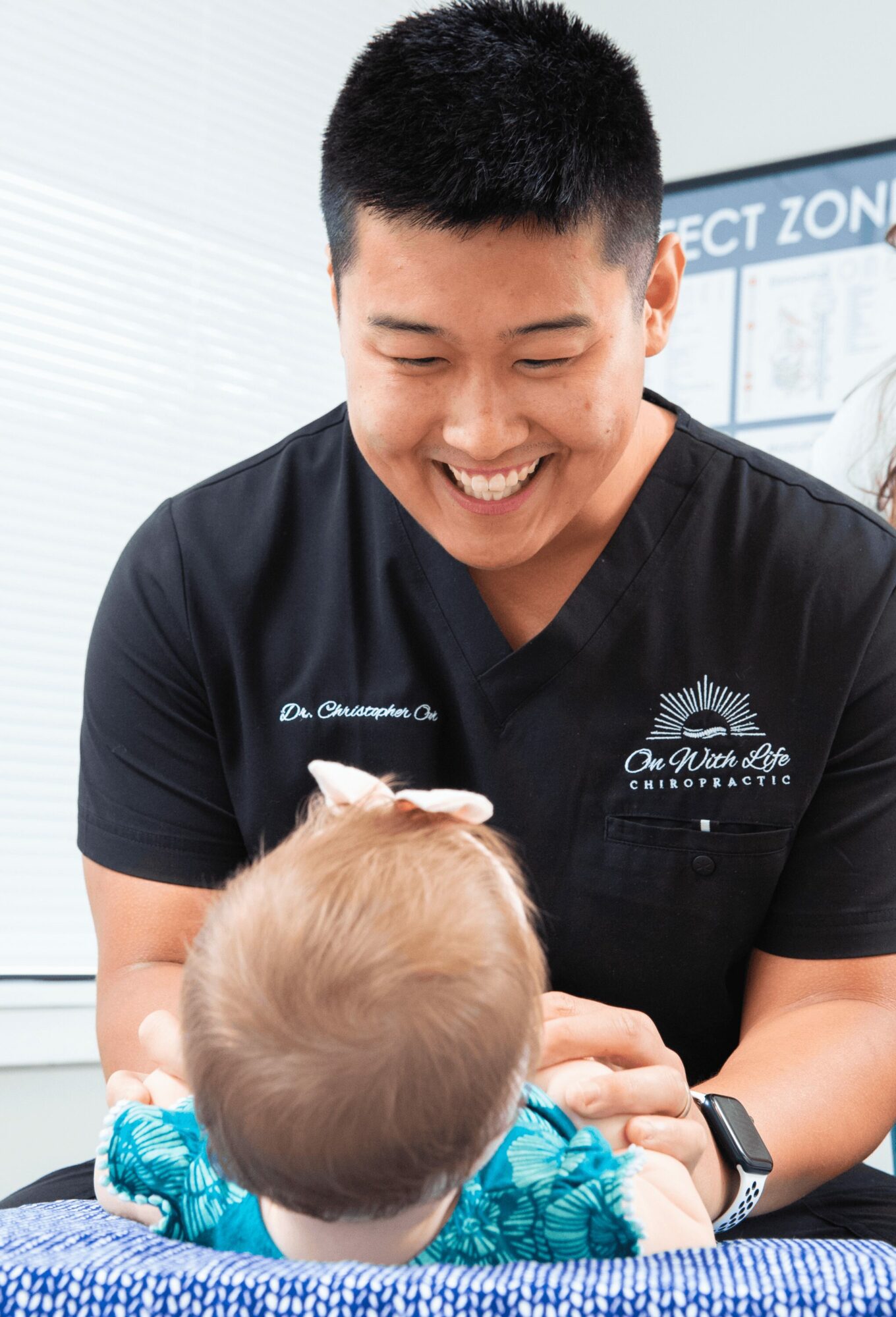 A smiling healthcare professional interacts with a young child in a clinical setting.