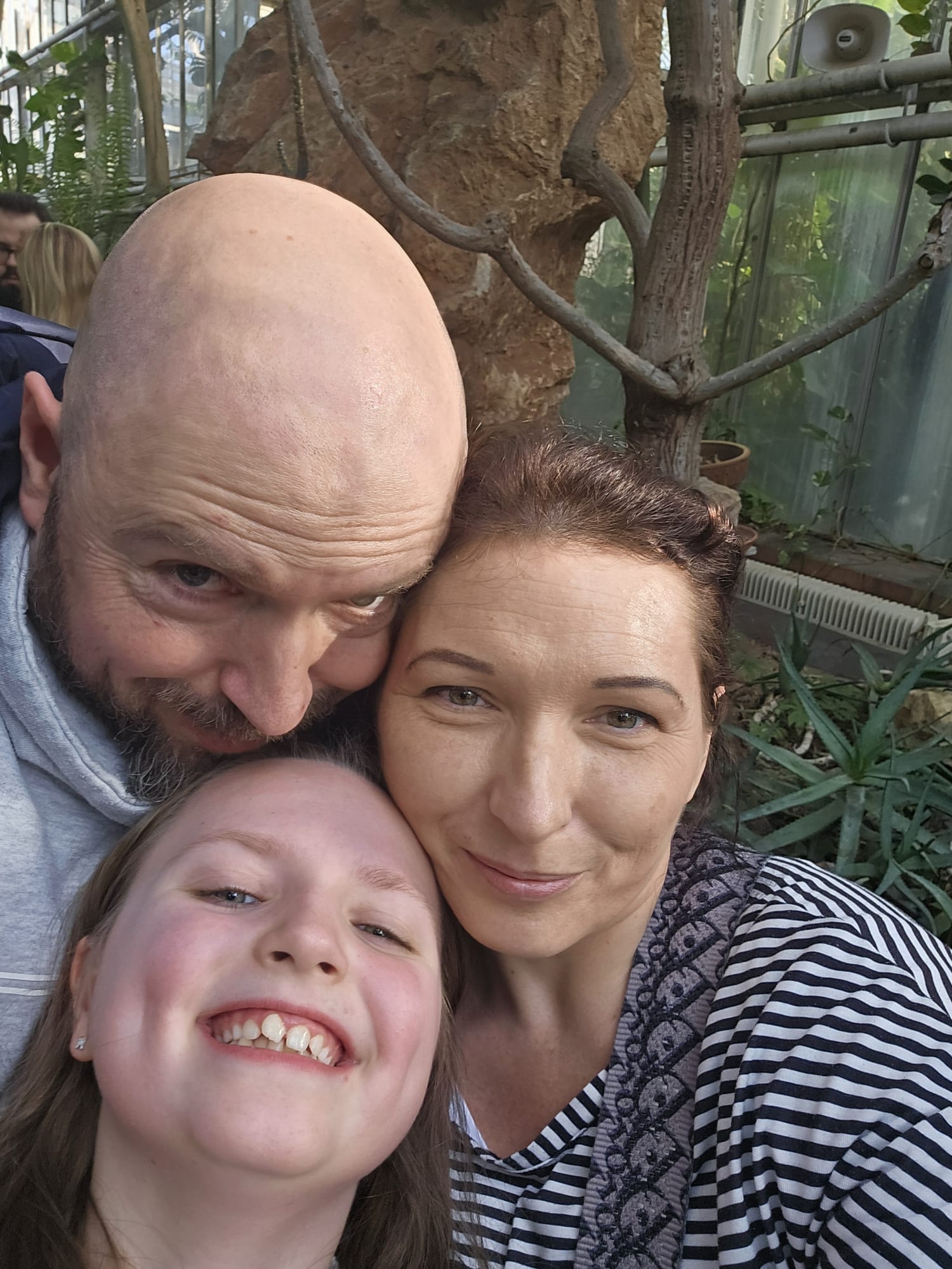 Three people smiling closely together in a lush, green environment with trees and plants.