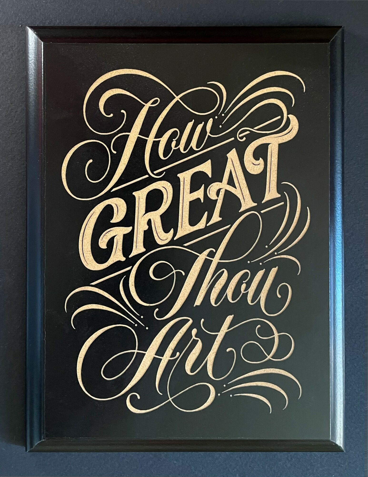 Framed artwork with decorative text reading 'How Great Thou Art' in elegant script, on a dark background.