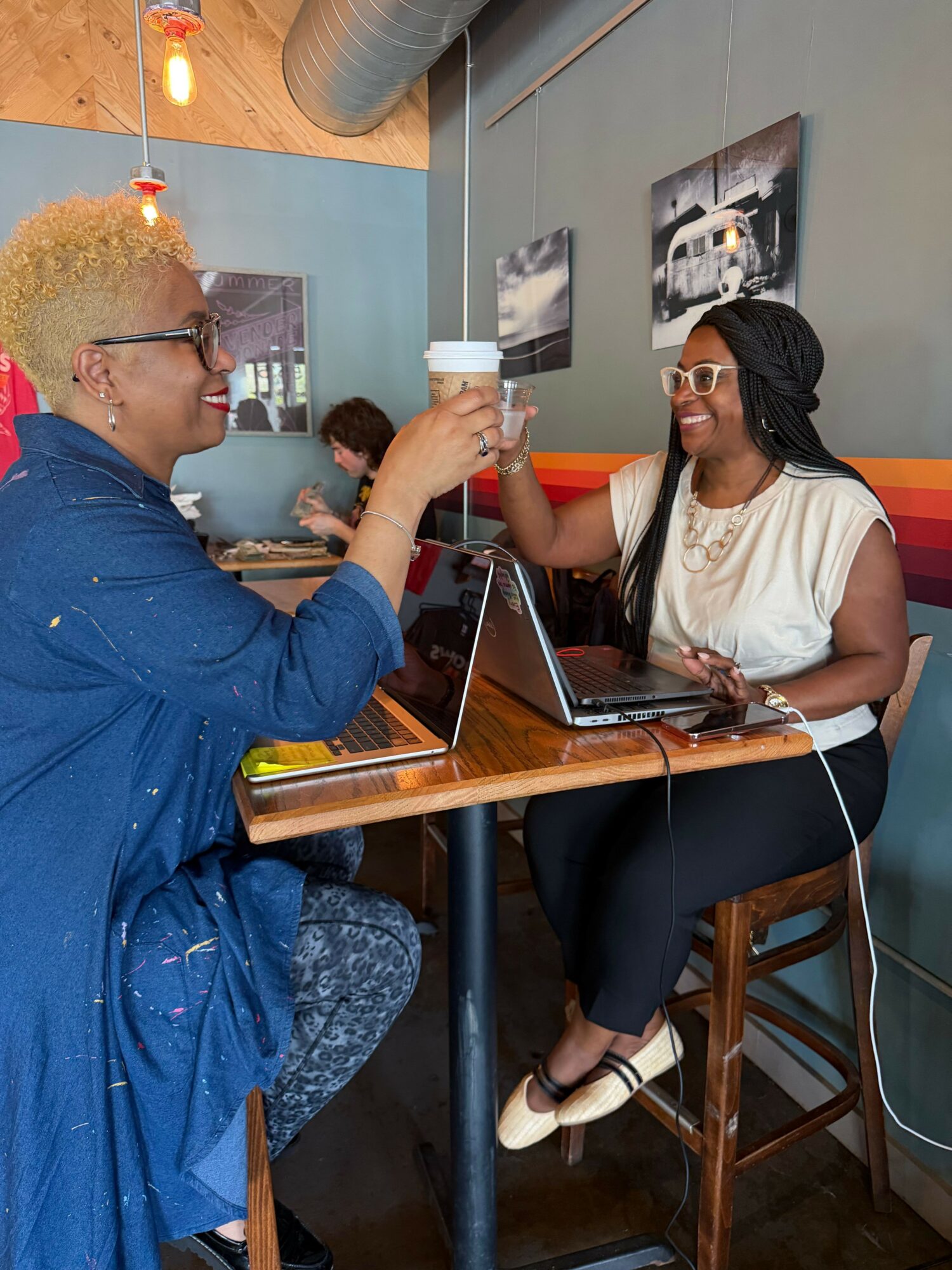 Person in blue shirt and glasses leaning over a table with a woman in white shirt and sunglasses sitting nearby.