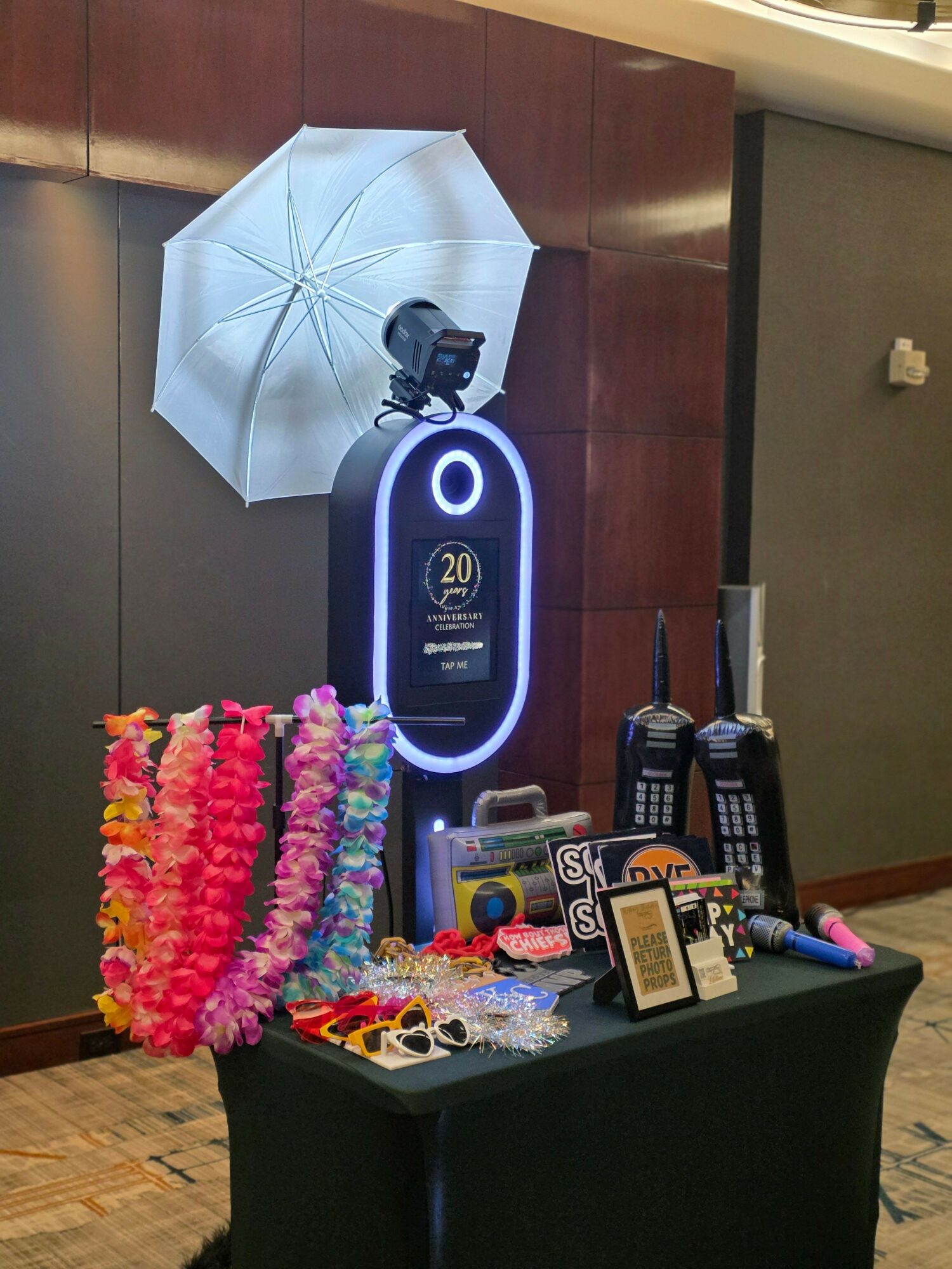 Photo of a table with a neon sign, drinks, and decorations, with a white umbrella attached to the wall behind.