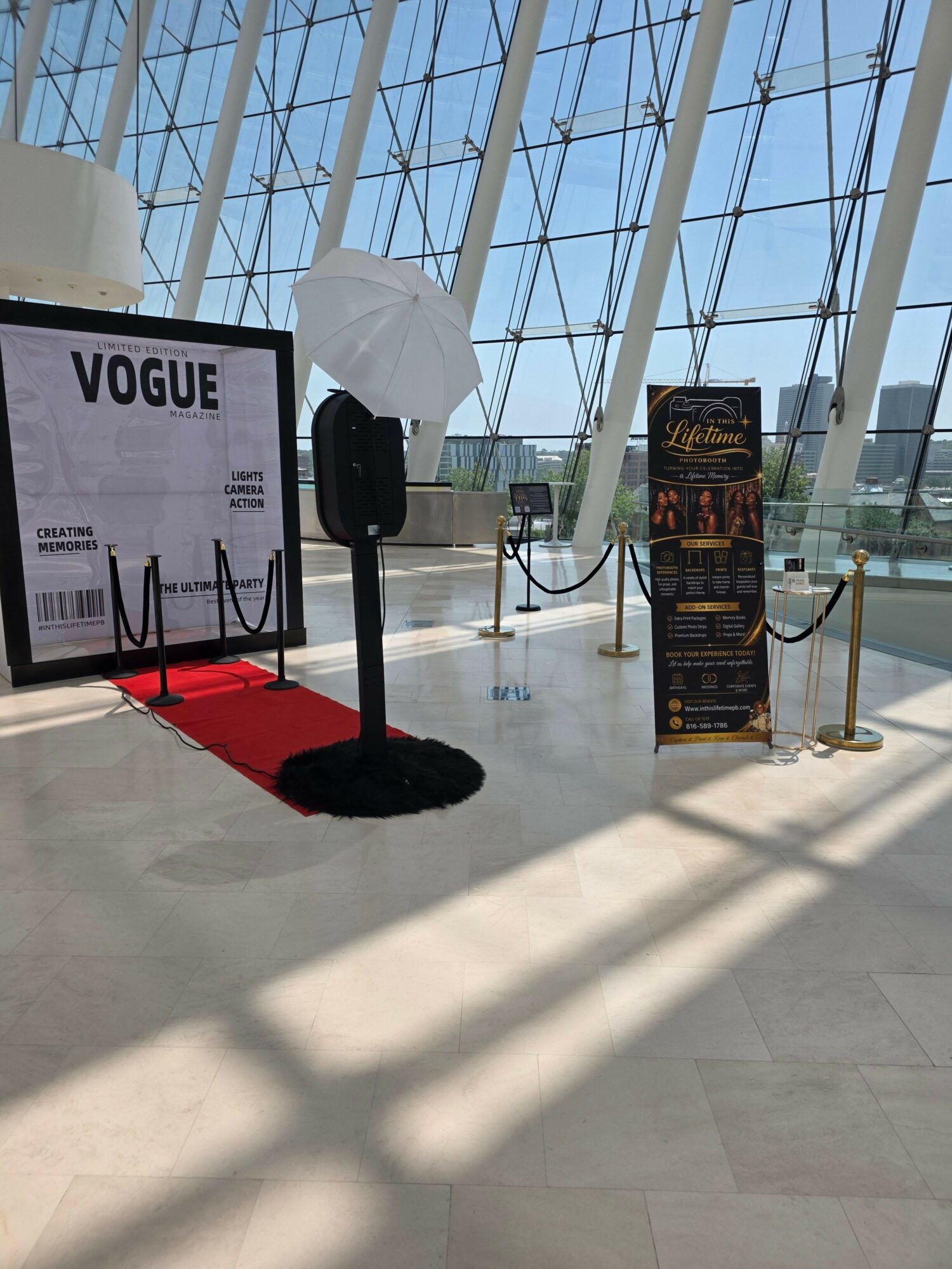 Indoor space with large glass windows, a table with a black rug, and promotional stands, sunlight casting shadows.