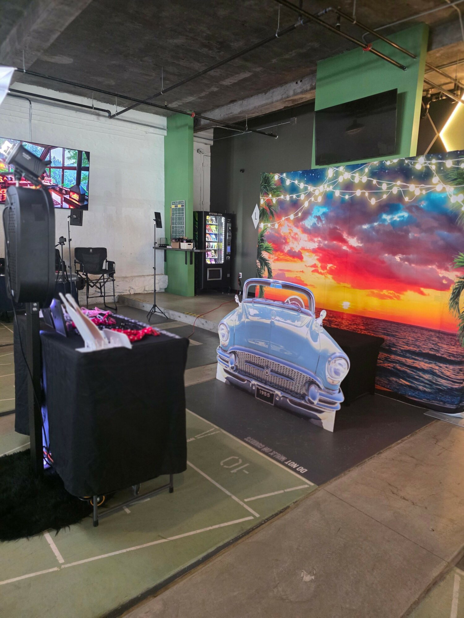 Indoor scene with a large colorful screen, a washing machine, and a table with a black cloth, viewed from the side.