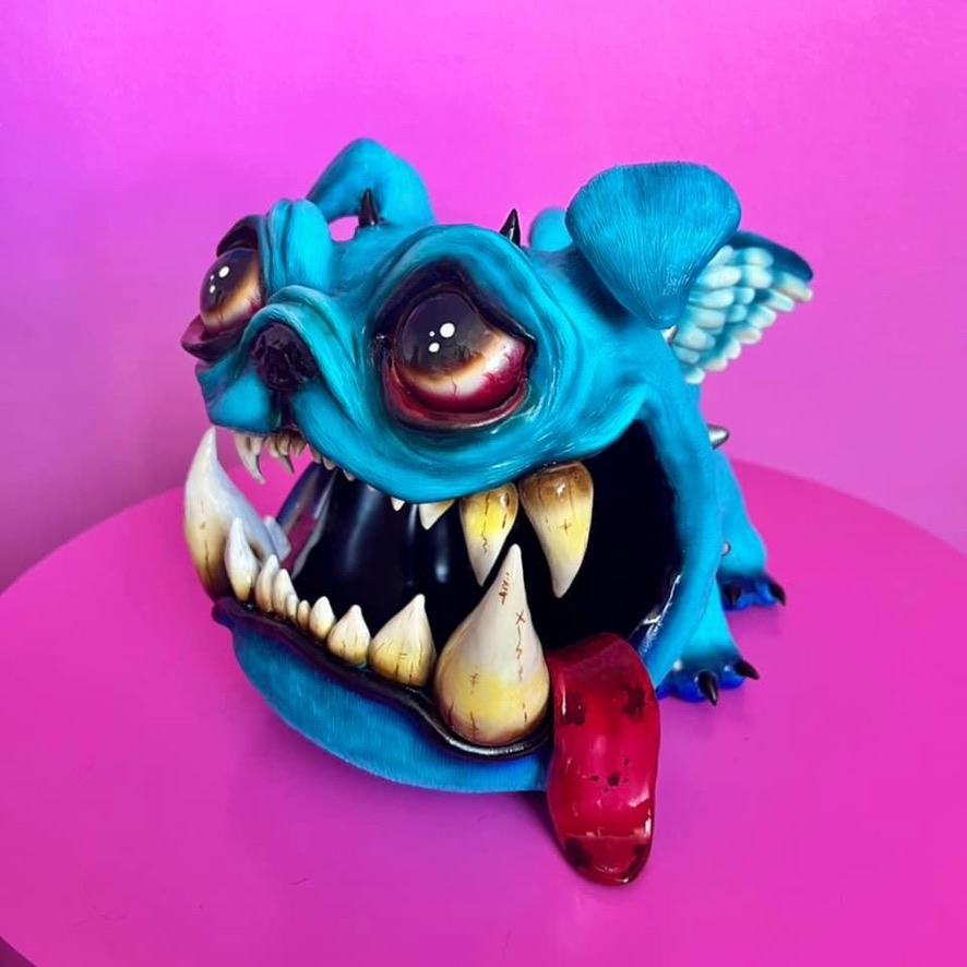 Colorful creature with large eyes, sharp teeth, and a red tongue on a pink surface with a pink background.