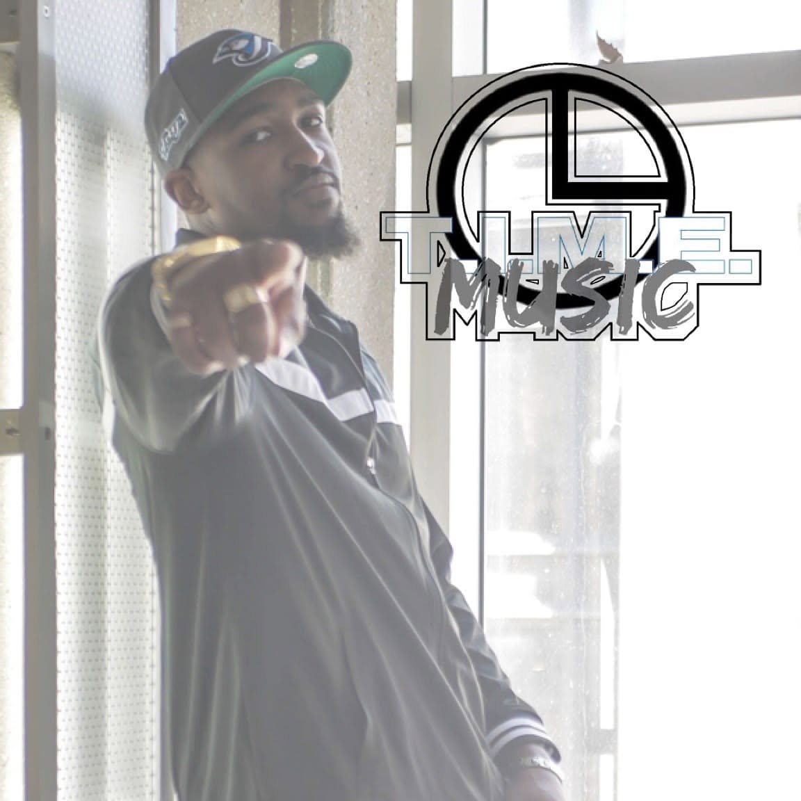 Man wearing a cap and jacket pointing at the camera, with a window in the background, and a logo with text overlay.
