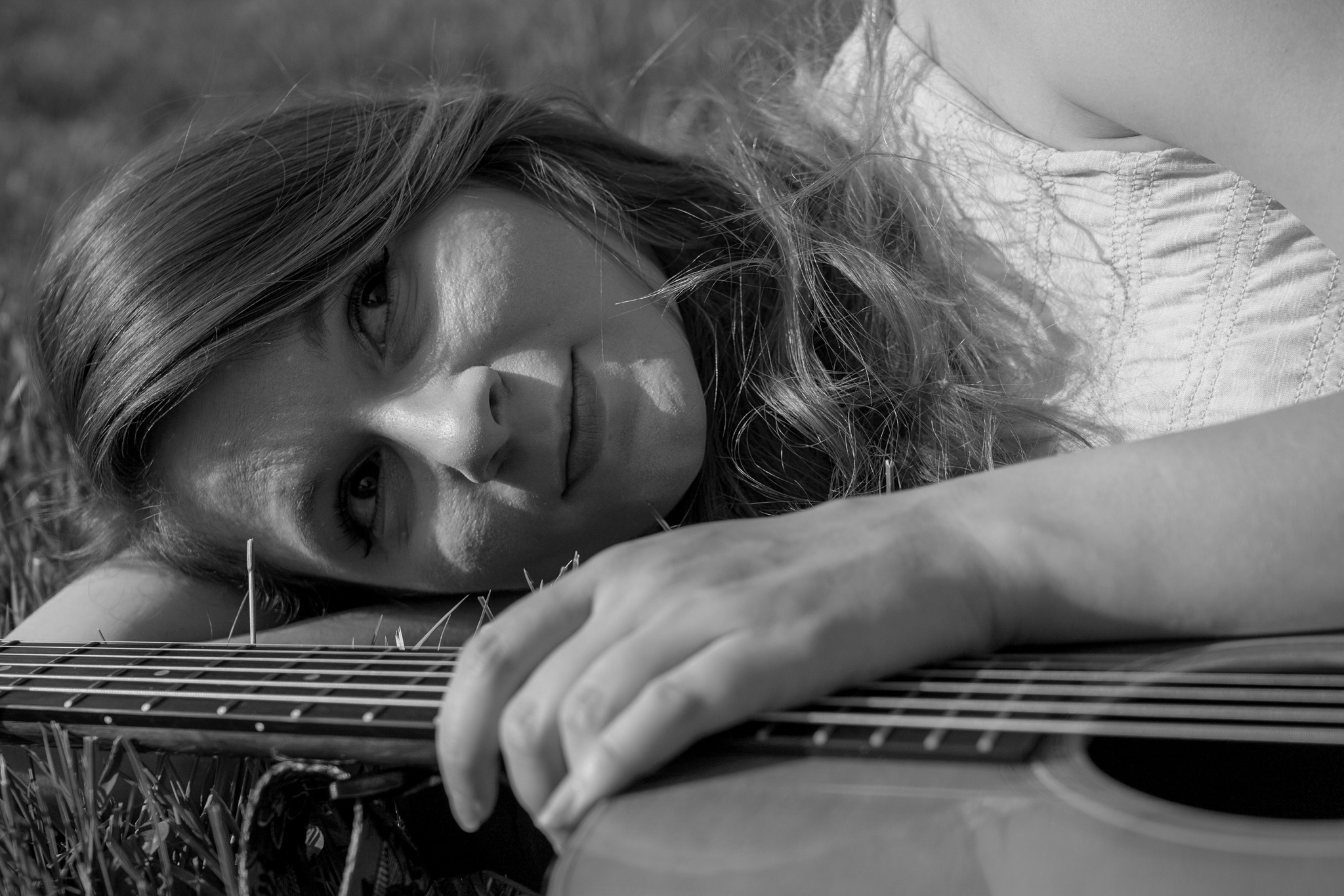 Woman lying down with her head resting on her arm, holding an acoustic guitar, in black and white.