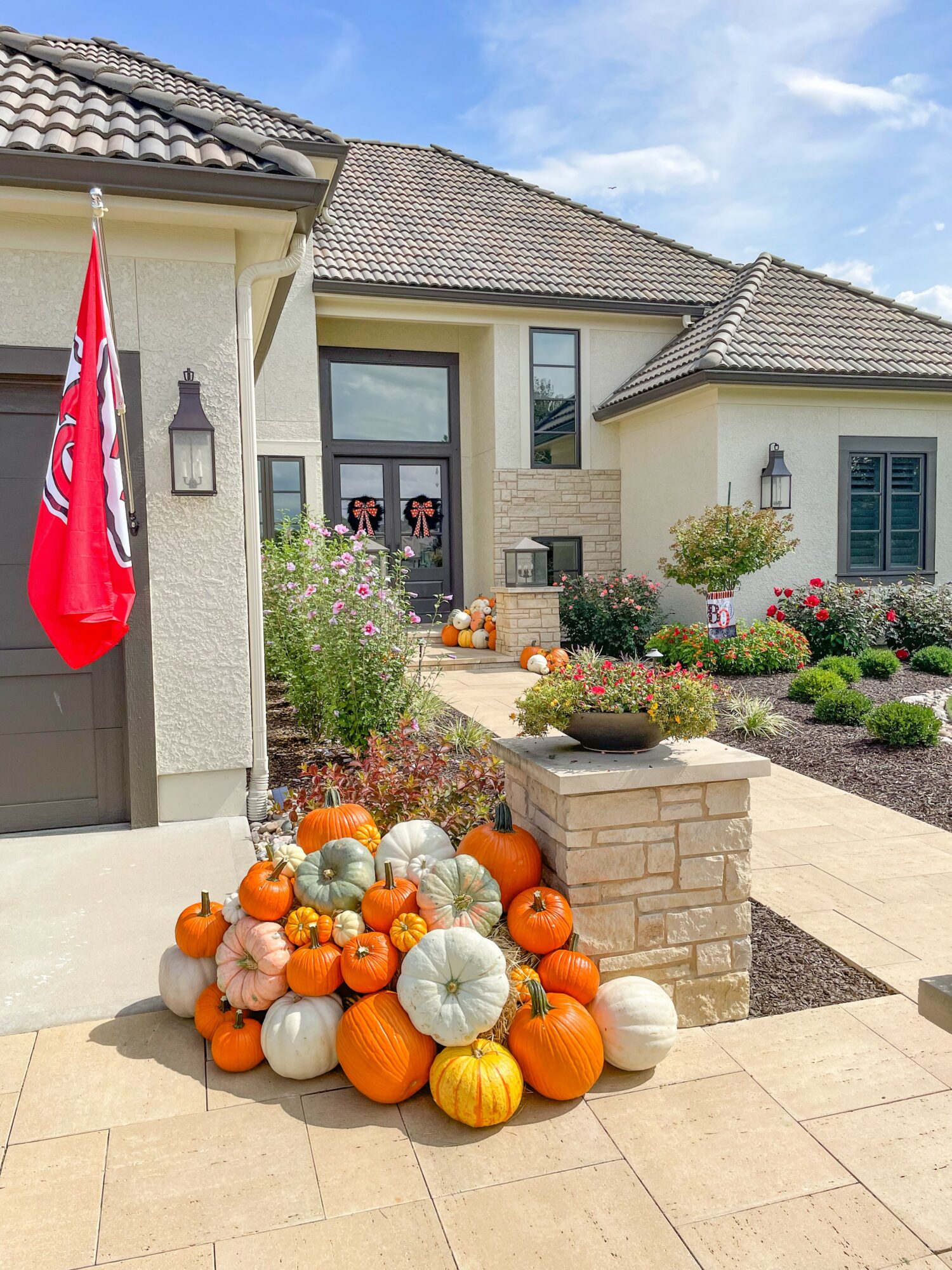 Pumpkins and gourds arranged outside a house with a garden and pathway, autumn decorations, clear sky.