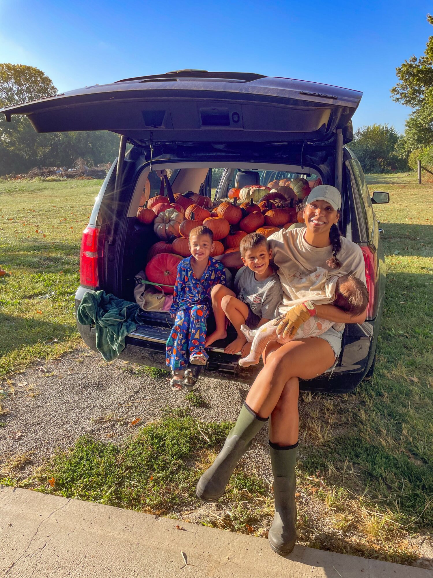 Woman and two children sitting at the back of a vehicle filled with apples outdoors on a sunny day.