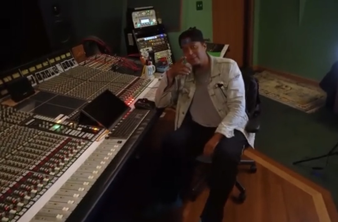 Person sitting in a recording studio with audio equipment, holding a phone to their ear, in a room with green walls.